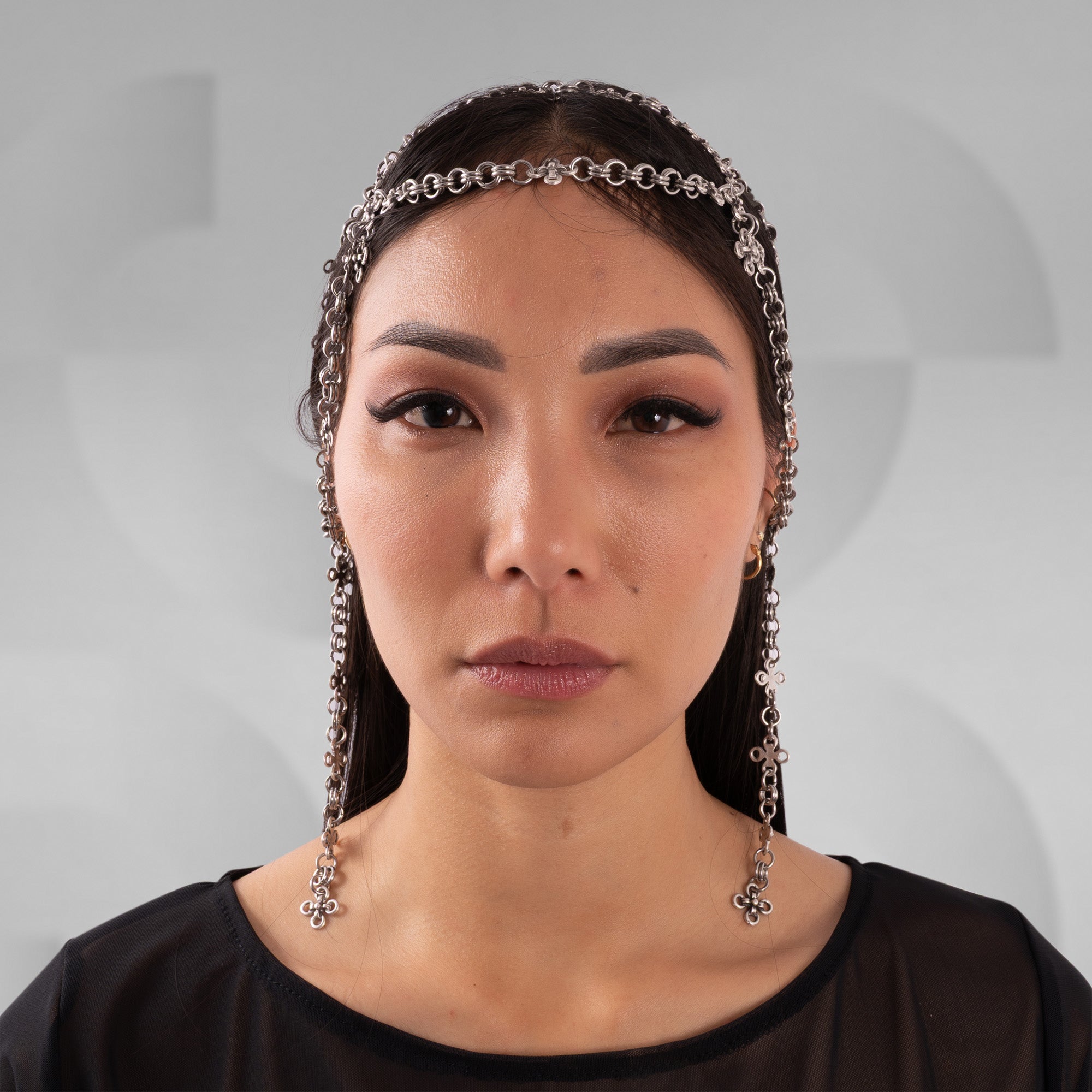 Woman wearing a headband with dangling chains against a gray background