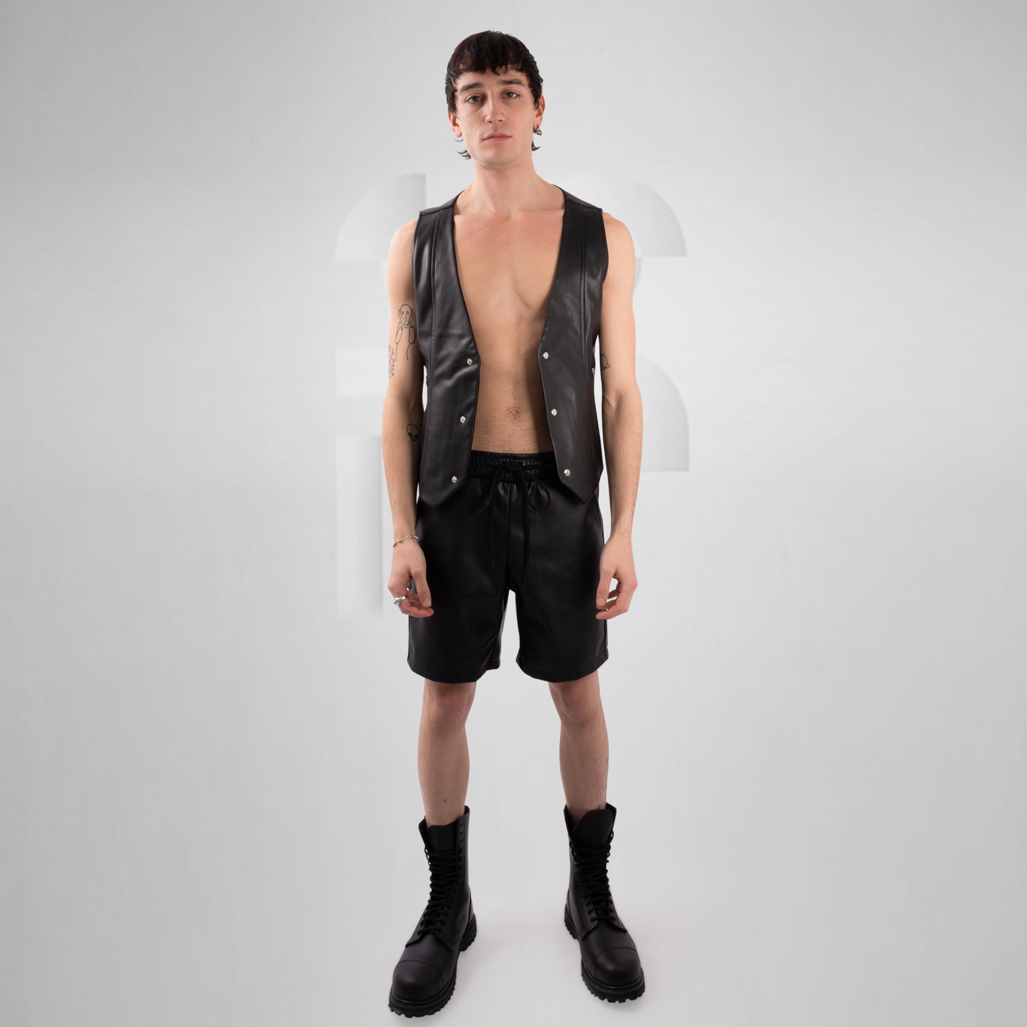 Person wearing a black leather vest, shorts, and boots on a white background