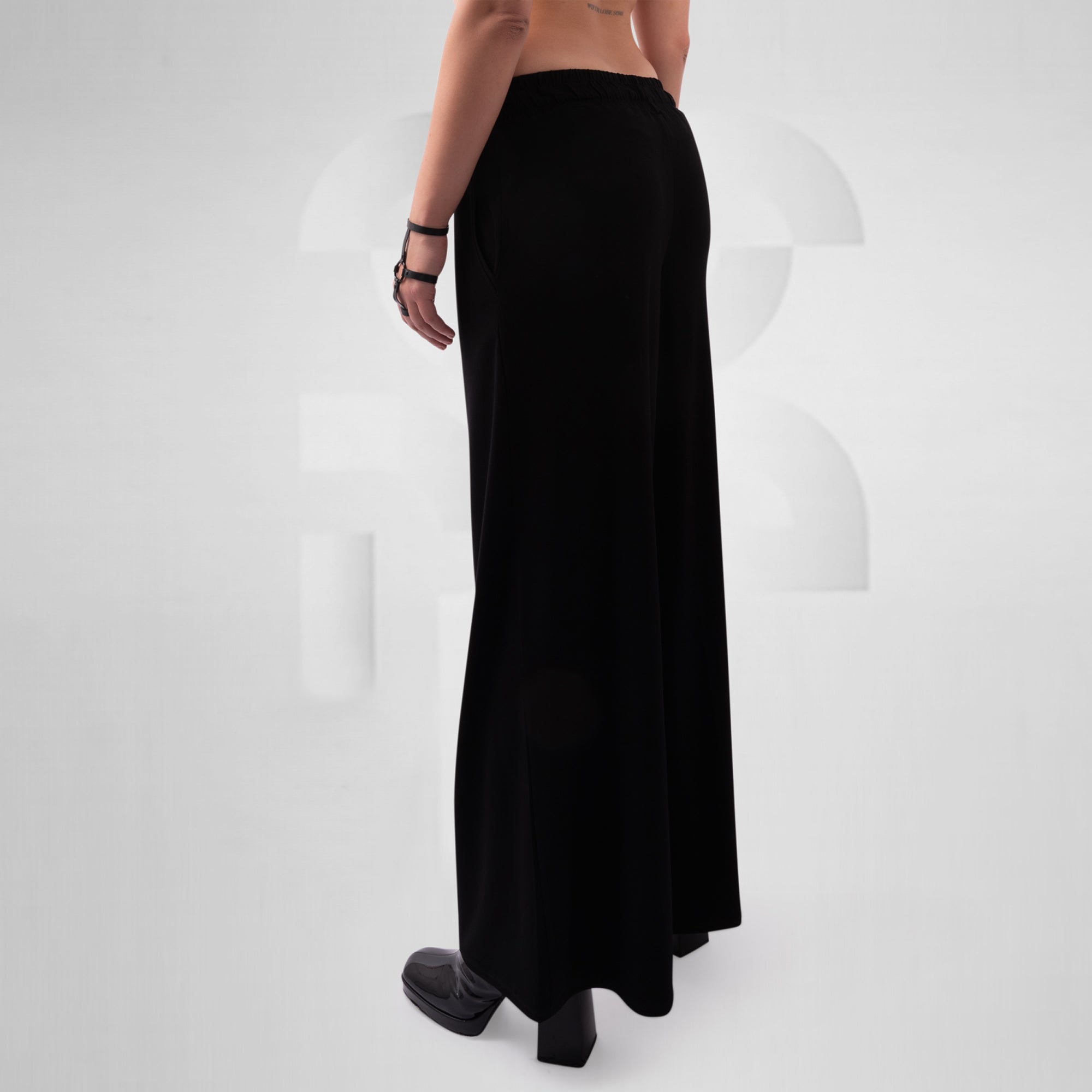 Black wide trousers worn by a person on a white background