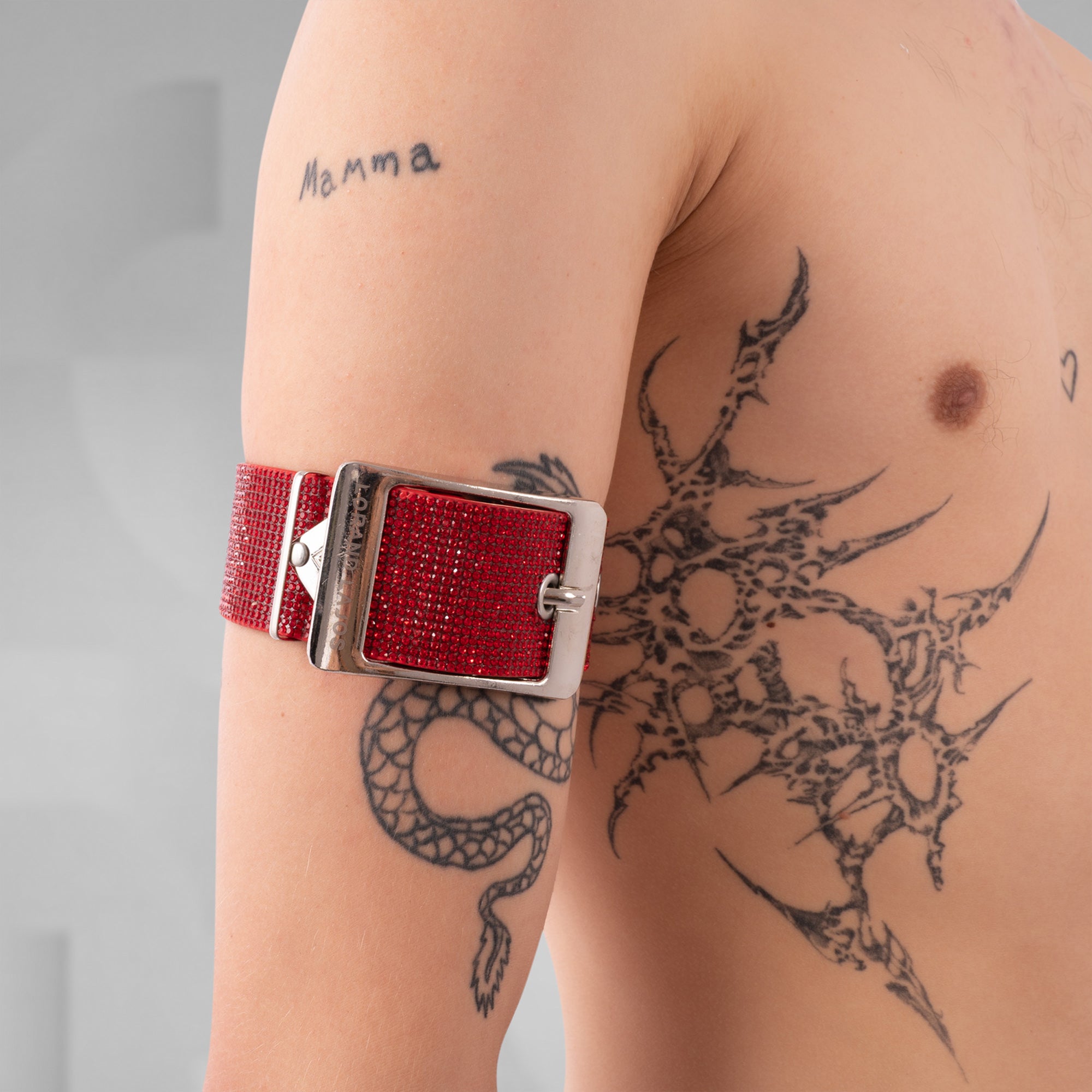 Red belt with silver buckle on a person's arm with tattoos