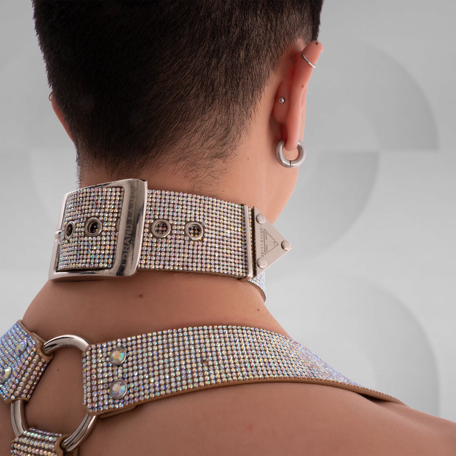 The image shows a close-up of a person wearing a sparkly choker with a large metallic ring in the center, complementing their bold tattoo. The choker has an eye-catching, glamorous design, making it a great accessory for standout fashion statements.