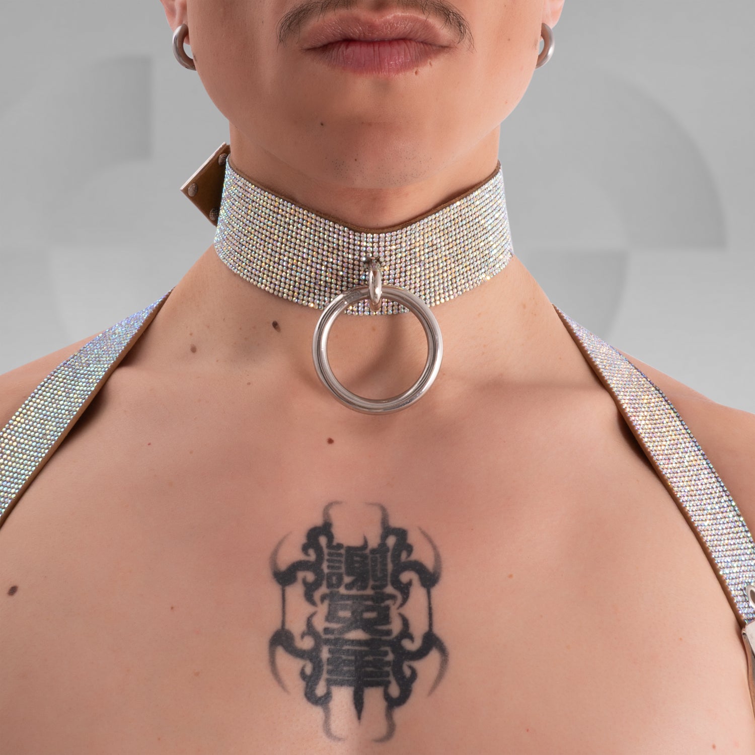 The image shows a close-up of a person wearing a sparkly choker with a large metallic ring in the center, complementing their bold tattoo. The choker has an eye-catching, glamorous design, making it a great accessory for standout fashion statements.