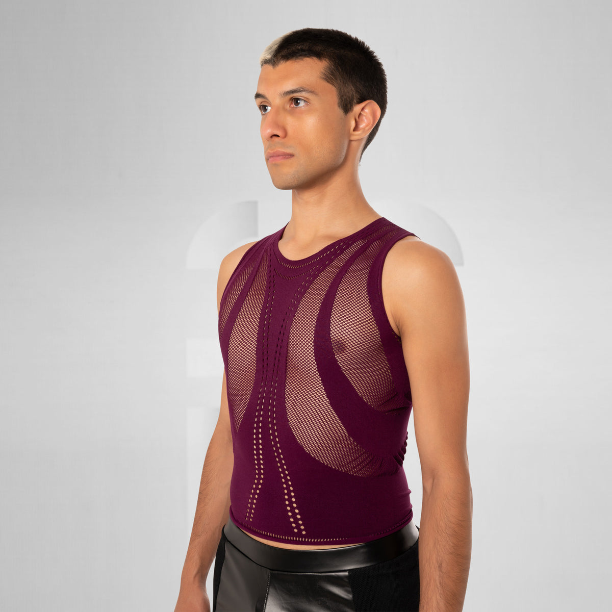 A man wearing a sleeveless, form-fitting knit top in deep burgundy with a distinctive open-knit pattern on the chest and waist, shown against a light gray studio background.