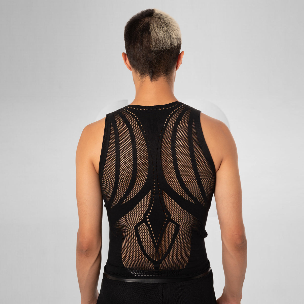 A man viewed from behind wearing a black sleeveless mesh back-support vest with a structured, ergonomic design on a light gray studio background.