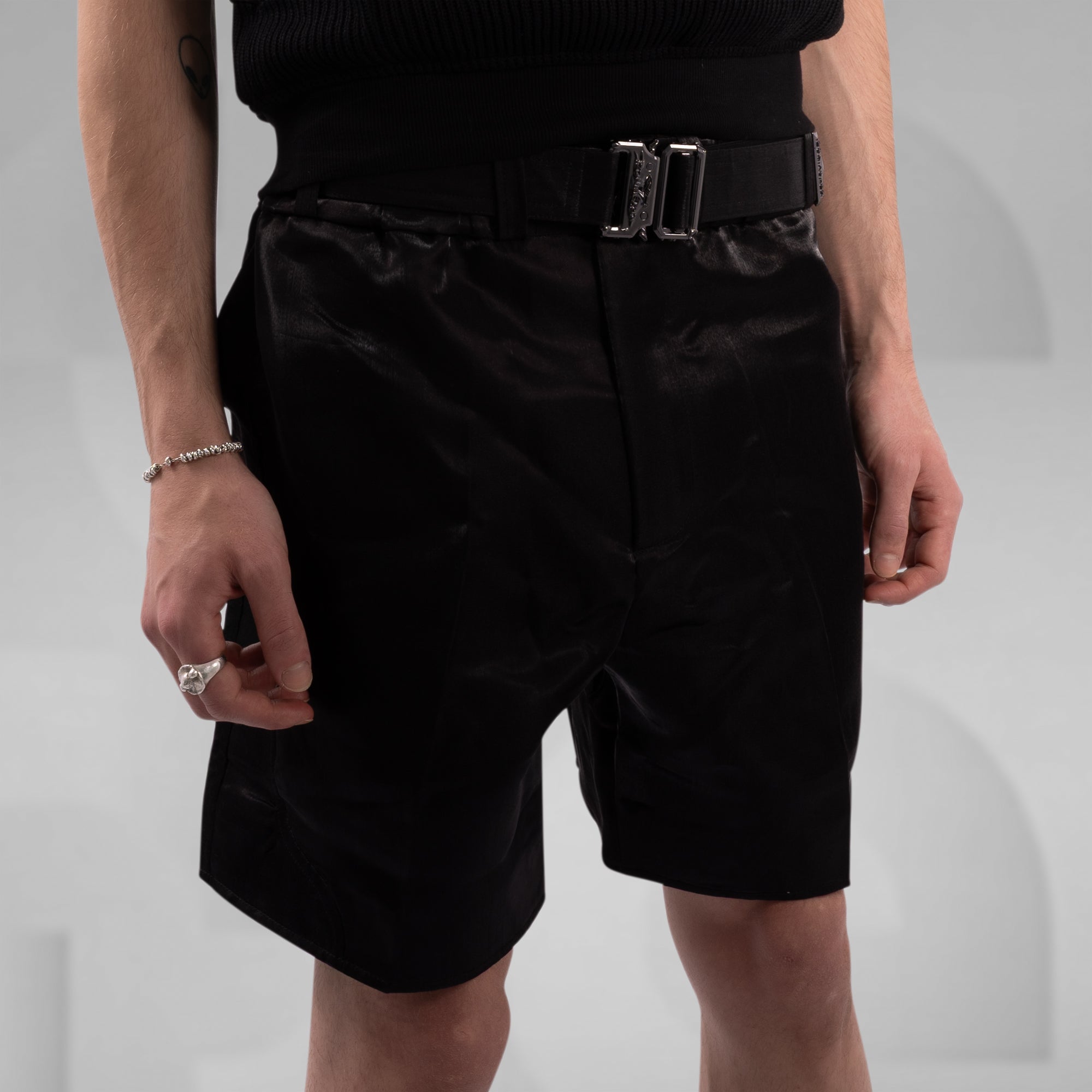 Person wearing black shorts with a belt on a plain background
