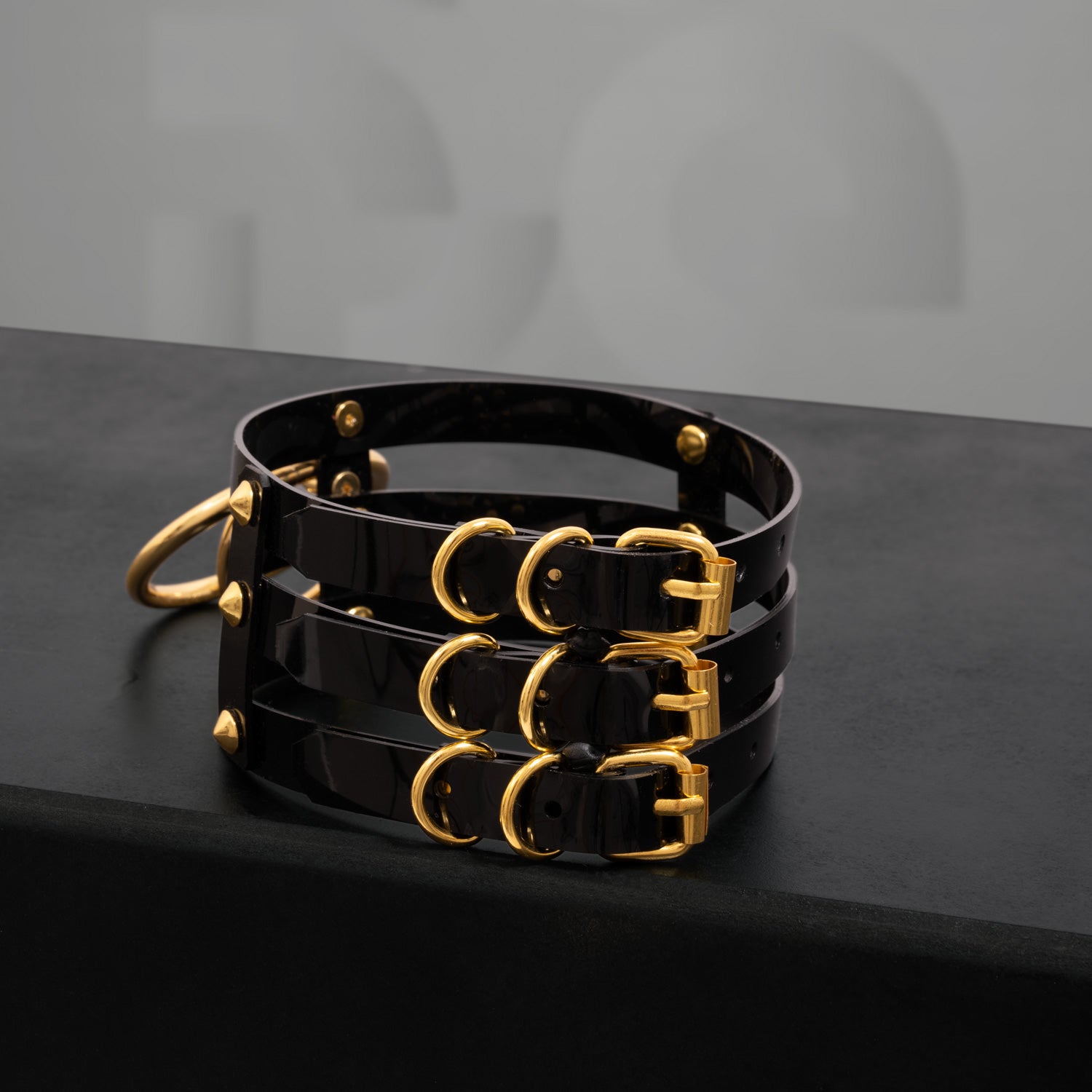 This image showcases a striking black PVC choker featuring three sleek stripes and adorned with metallic spikes. The design includes two bold rings at the front, adding an edgy yet elegant touch. The high-gloss finish of the PVC enhances its modern aesthetic, making it a perfect accessory for both nightlife and everyday outfits. This choker is designed to make a statement while blending a sense of daring style with sophistication.