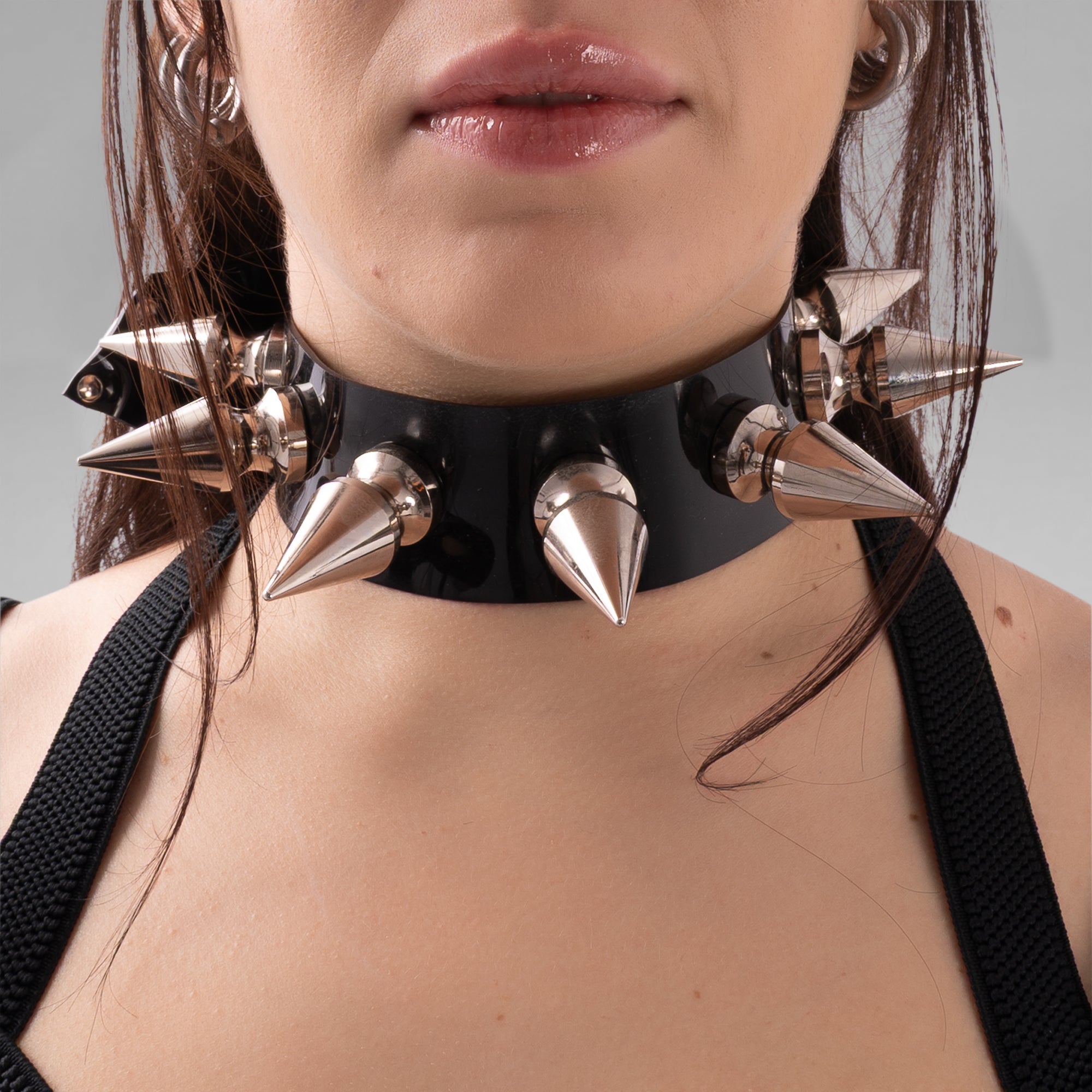 Close-up of a person wearing a black leather choker with metallic spikes on a neutral background