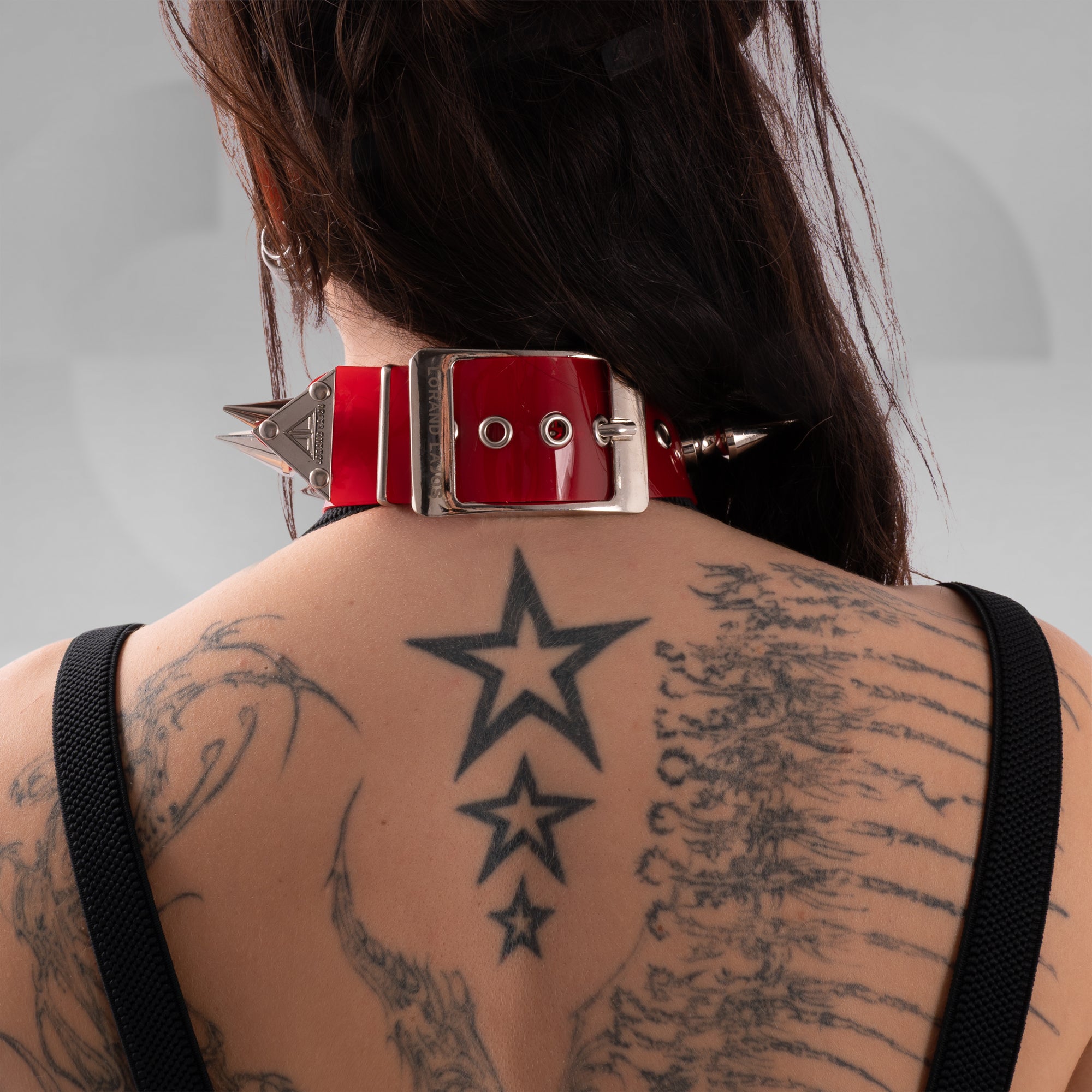 Person wearing a red and silver choker with spikes on a gray background