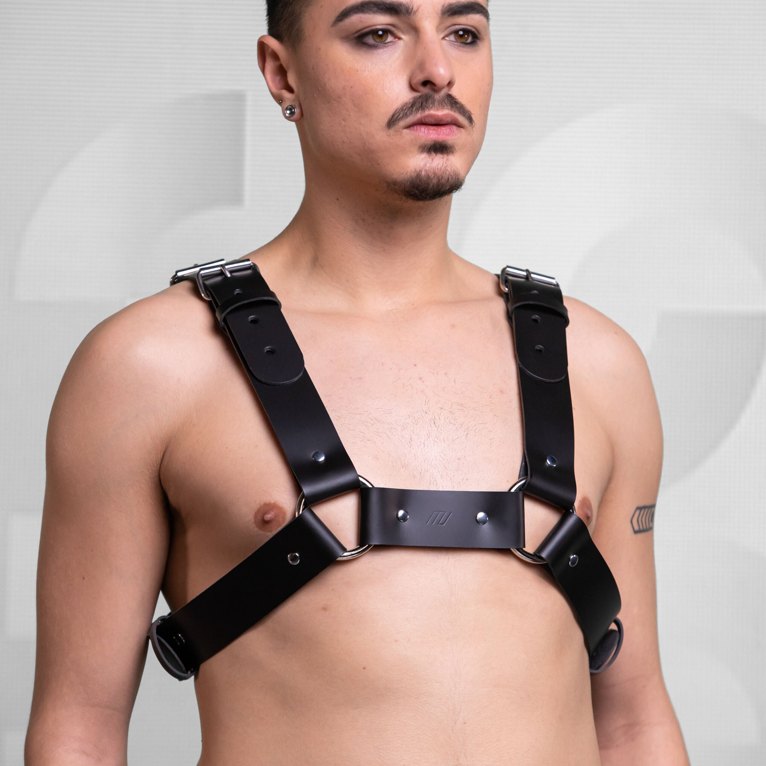 striking black leather harness paired with a flowy black skirt. The harness features bold straps and metallic accents, creating an edgy aesthetic. The look is complemented by the neutral background, emphasizing the outfit's unique combination of strength and style.