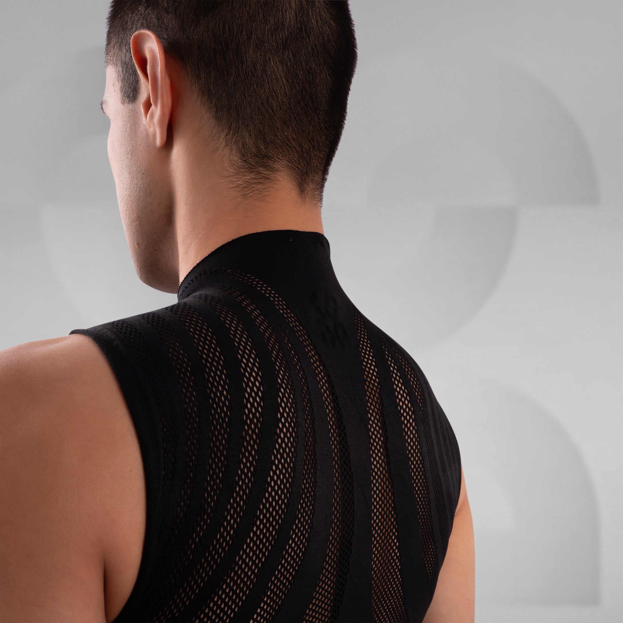 Man wearing a black sleeveless top with mesh design on a gray background