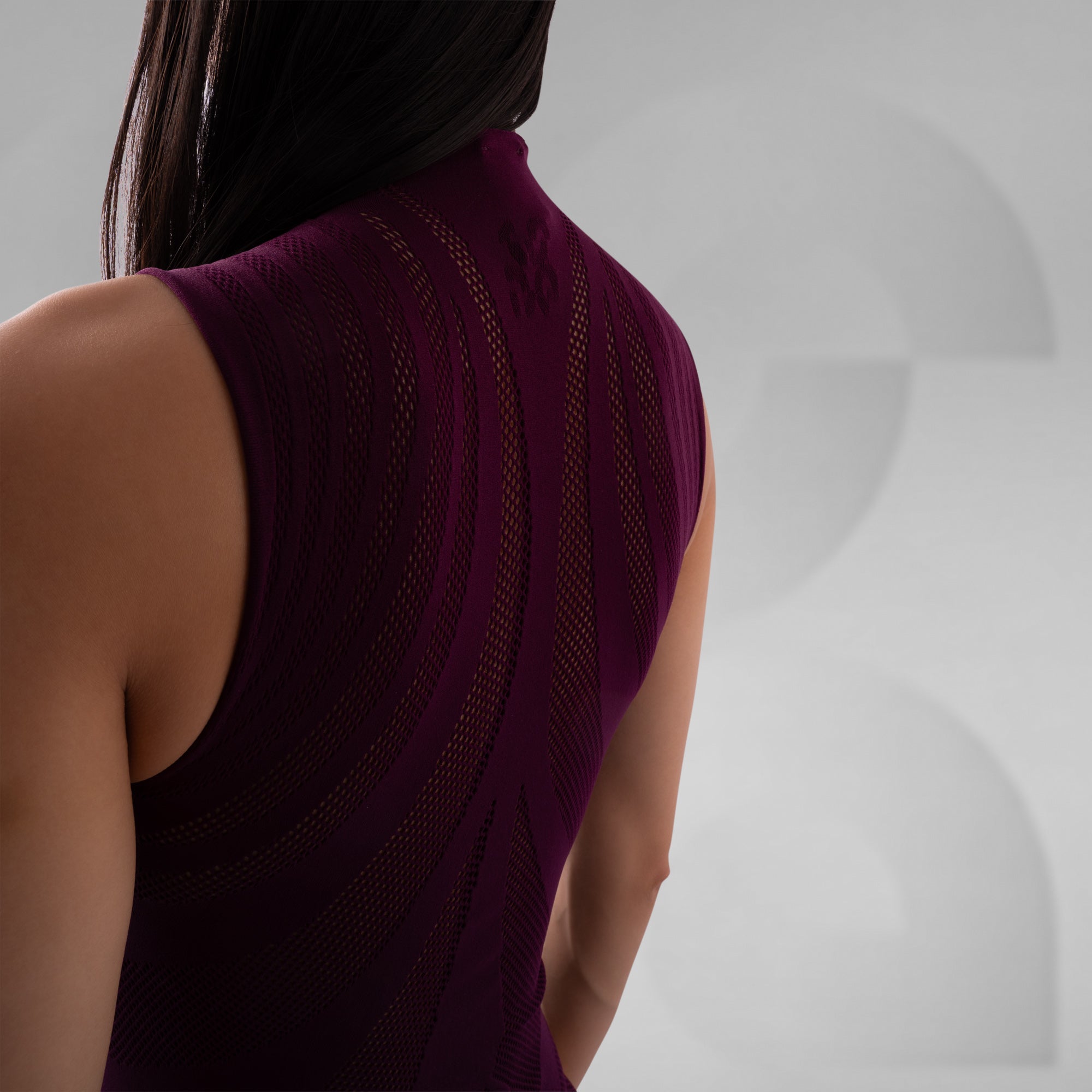 Person wearing a dark purple sleeveless top against a neutral background