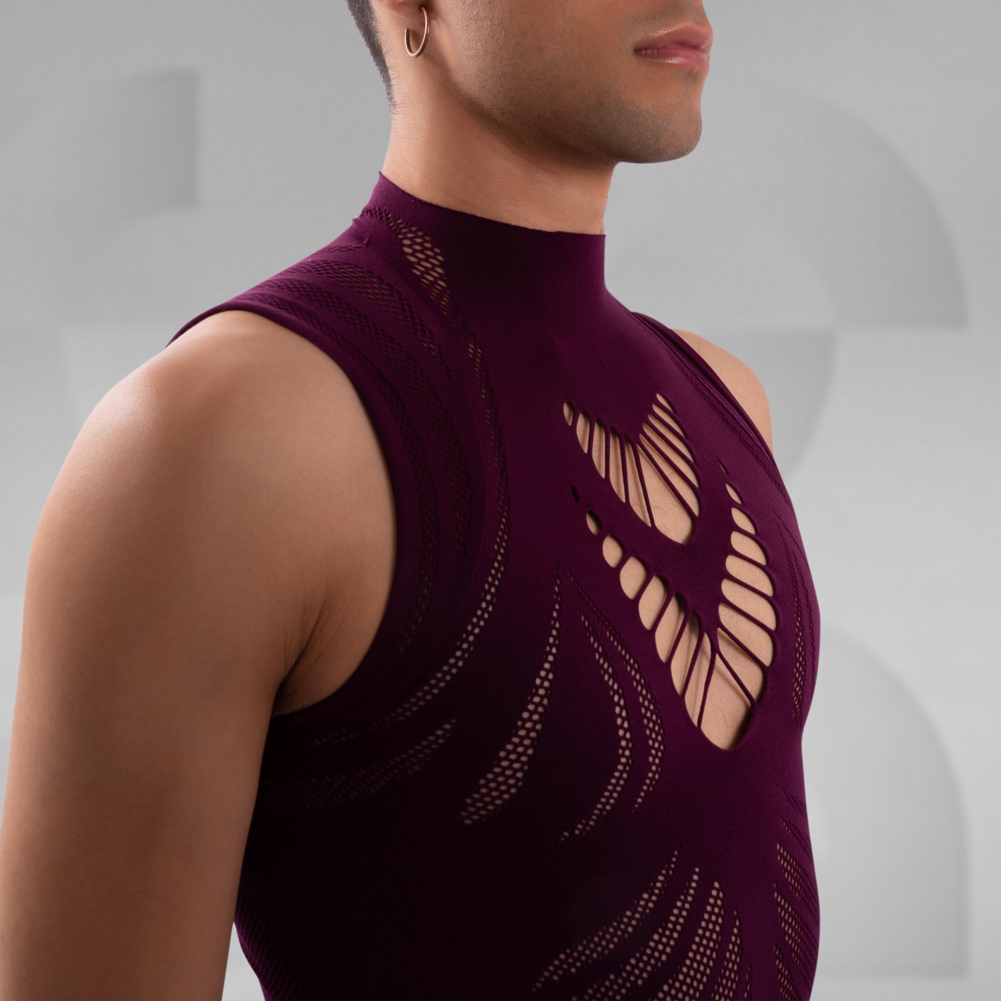 Man wearing a maroon sleeveless top with cut-out design on a gray background