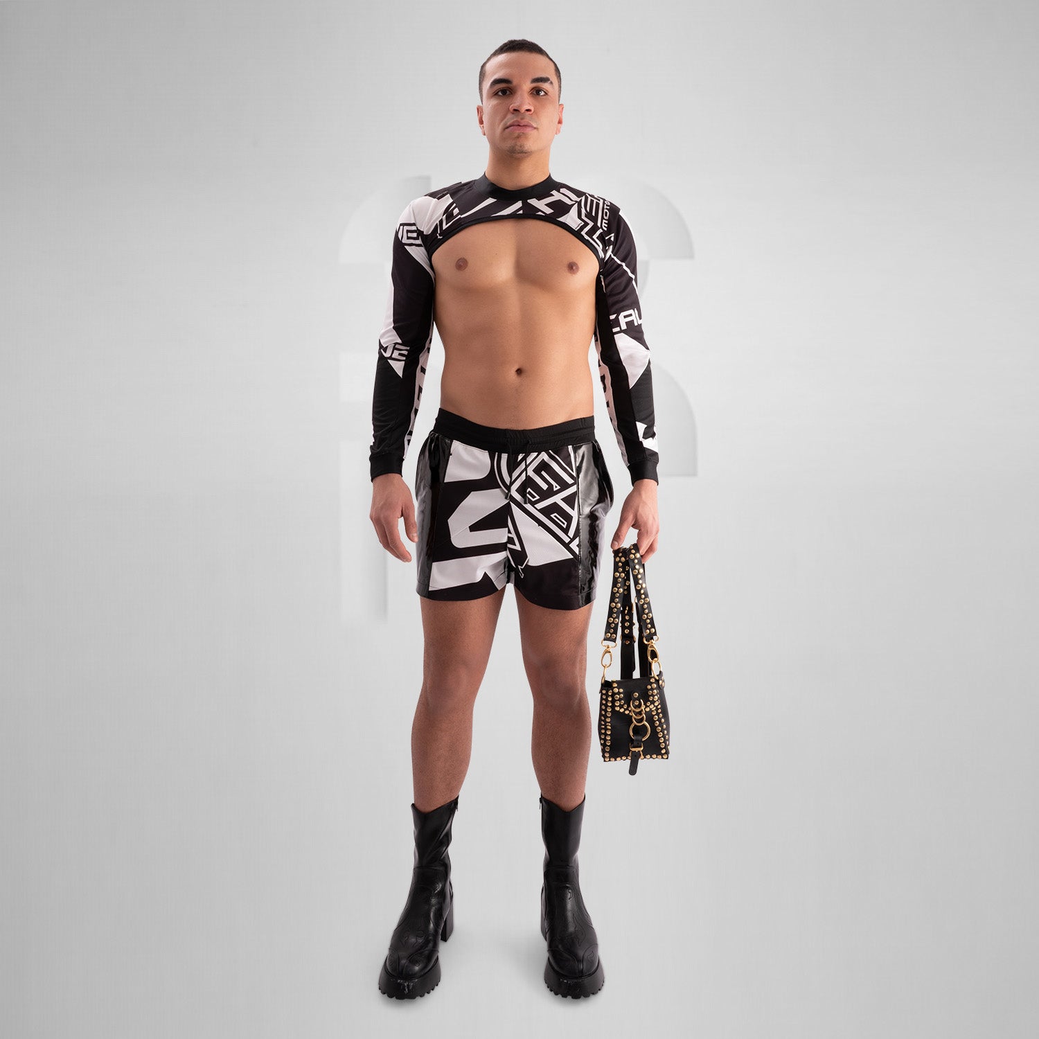 This image features a person wearing a unique and edgy outfit. The top is minimal and metallic, resembling a harness, while the skirt has bold black and white geometric designs. The outfit is completed with tall, shiny black thigh-high boots. The styling appears to be avant-garde and fashion-forward.