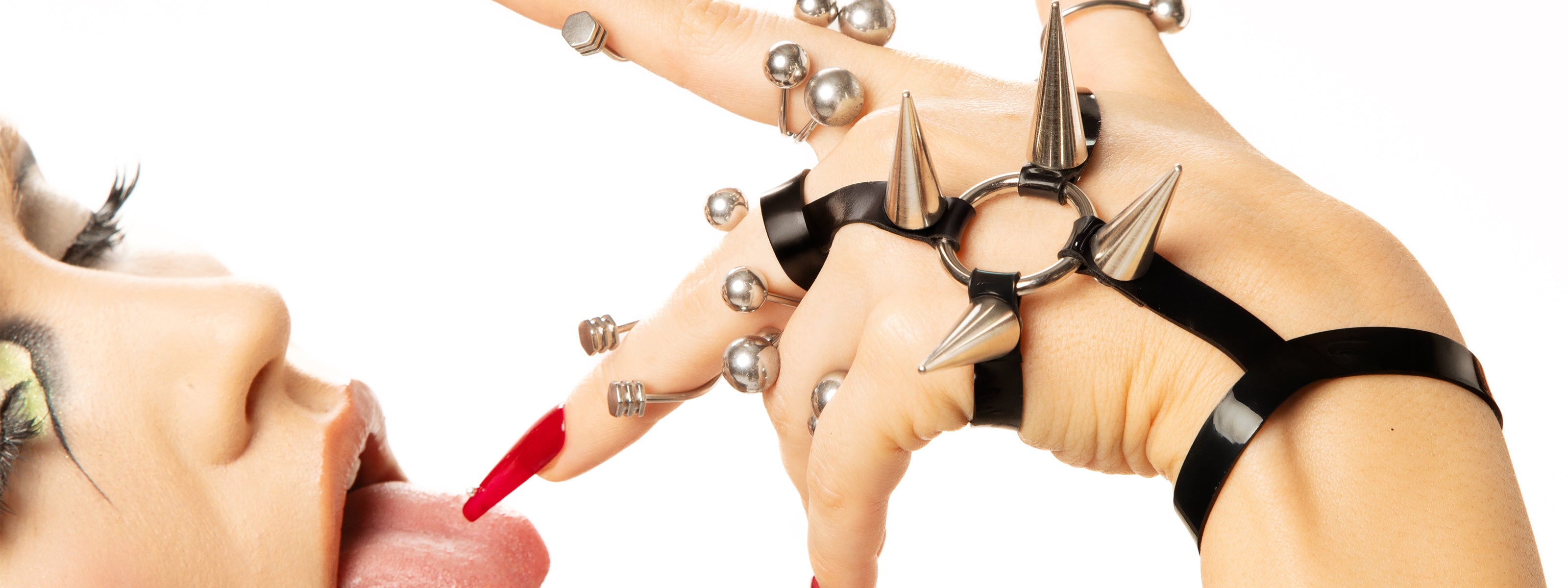 an array of striking and edgy rings, complemented by a sleek latex hand harness, provocatively draws attention to the mouth of another girl. This bold gesture intertwines fashion and allure, creating an intriguing moment that captivates the eye.