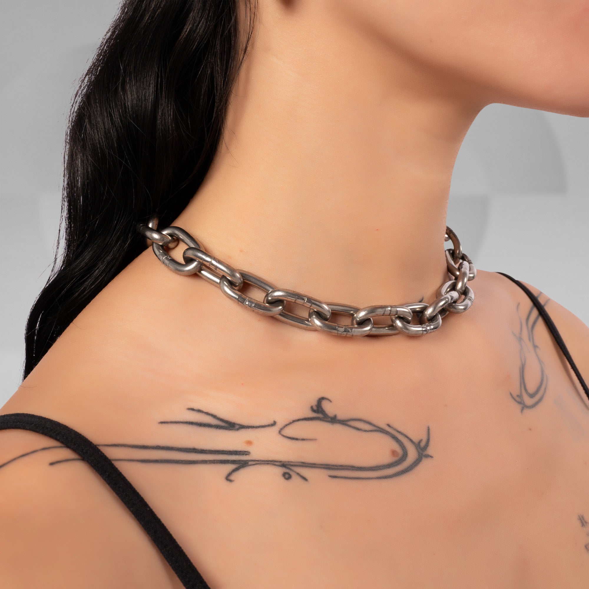 A close-up of a model's neck and upper chest wearing a chunky, polished silver chain choker necklace.