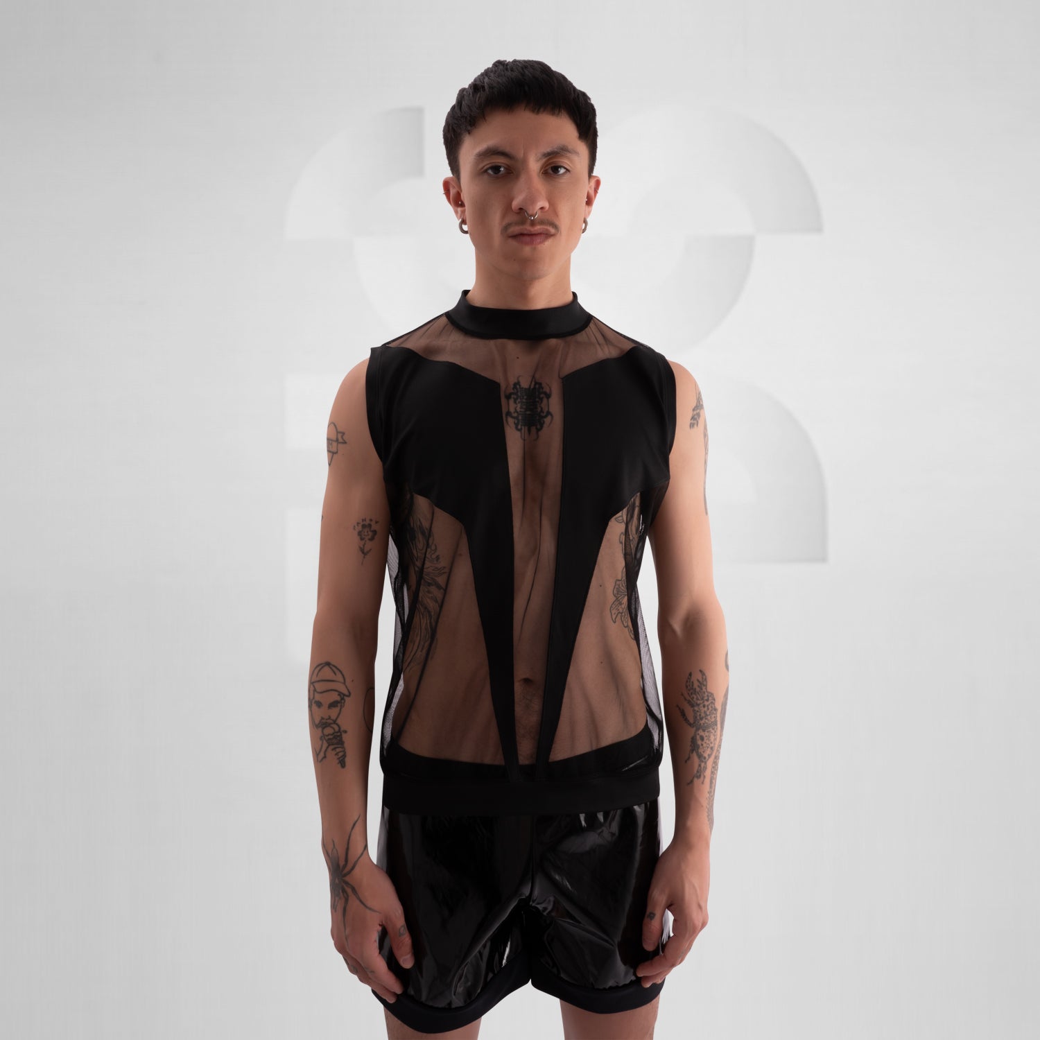 The image showcases a person wearing a bold fashion ensemble featuring a sheer black top with geometric patterns and solid black accents, paired with black shorts. The overall look is edgy and avant-garde, great for a fashion-forward statement.