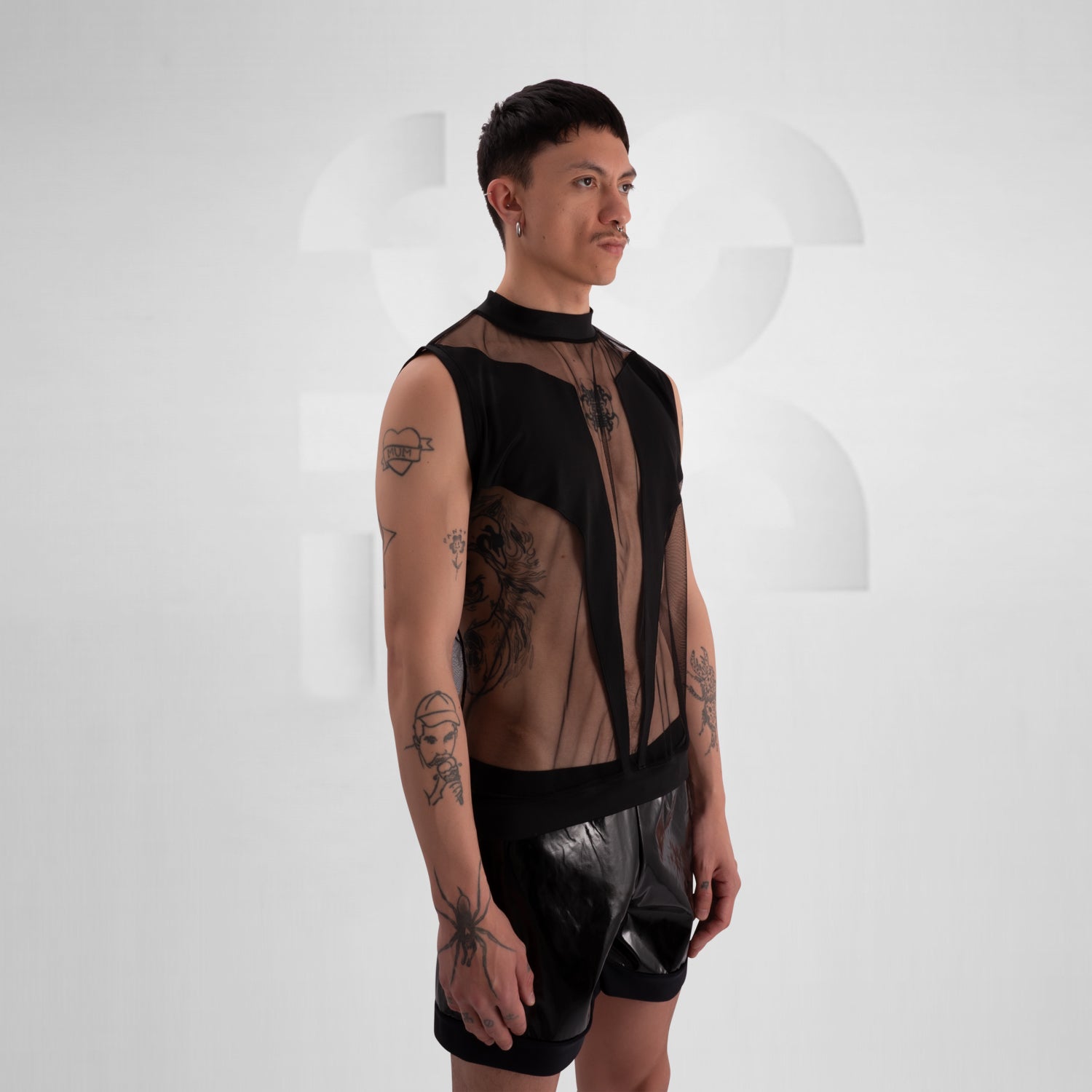 The image showcases a person wearing a bold fashion ensemble featuring a sheer black top with geometric patterns and solid black accents, paired with black shorts. The overall look is edgy and avant-garde, great for a fashion-forward statement.