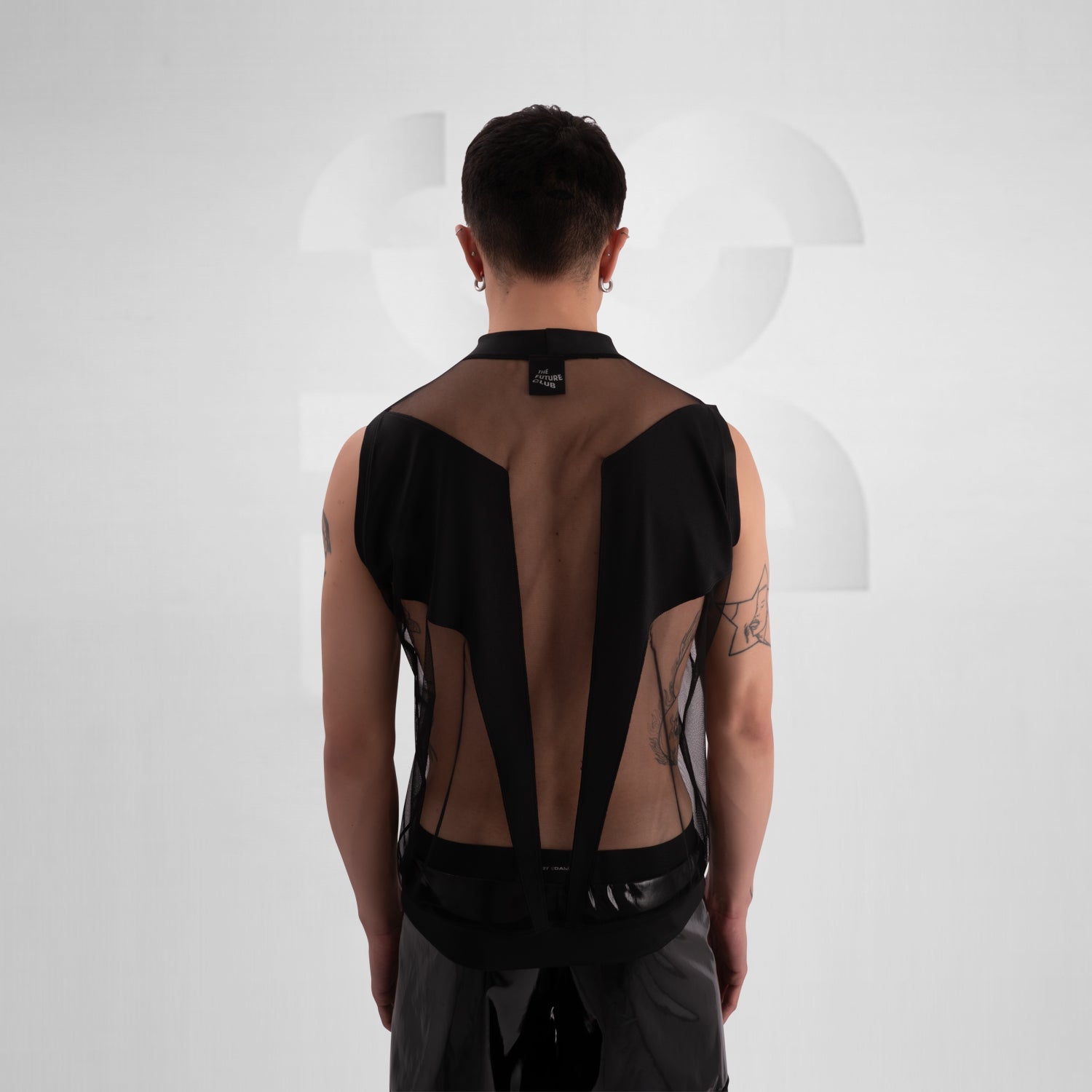 The image showcases a person wearing a bold fashion ensemble featuring a sheer black top with geometric patterns and solid black accents, paired with black shorts. The overall look is edgy and avant-garde, great for a fashion-forward statement.