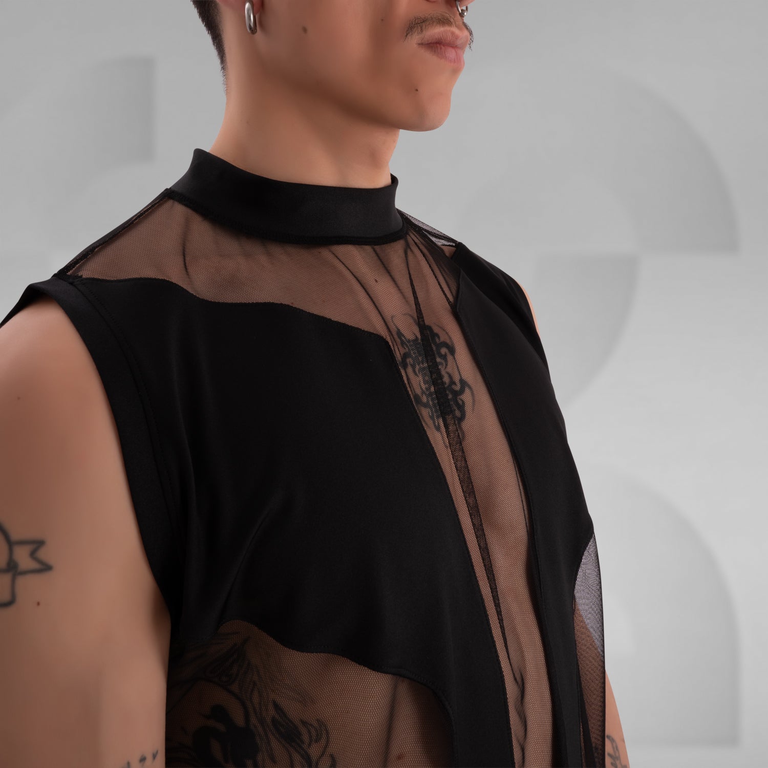 The image showcases a person wearing a bold fashion ensemble featuring a sheer black top with geometric patterns and solid black accents, paired with black shorts. The overall look is edgy and avant-garde, great for a fashion-forward statement.