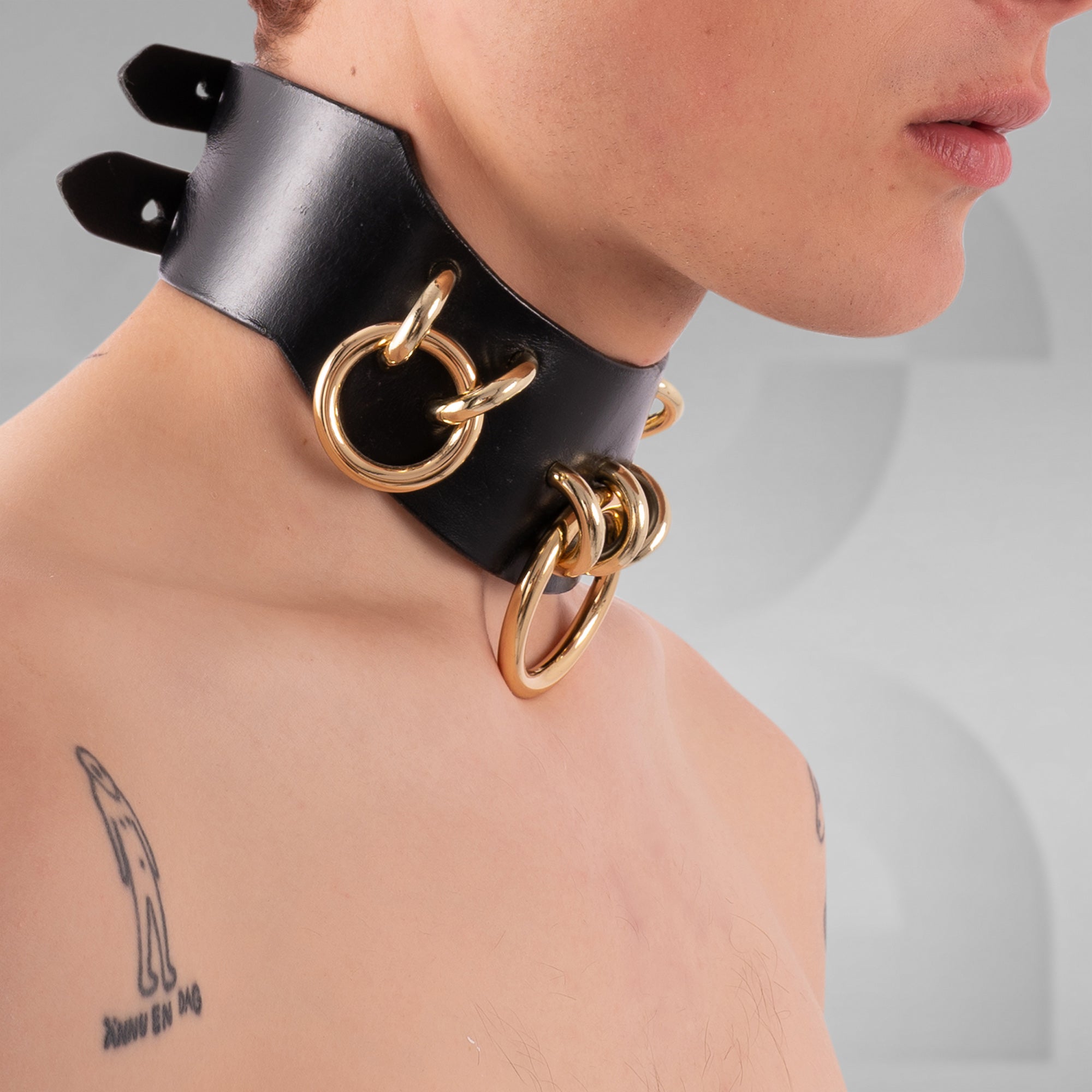 Black leather choker with gold rings worn by a person on a neutral background