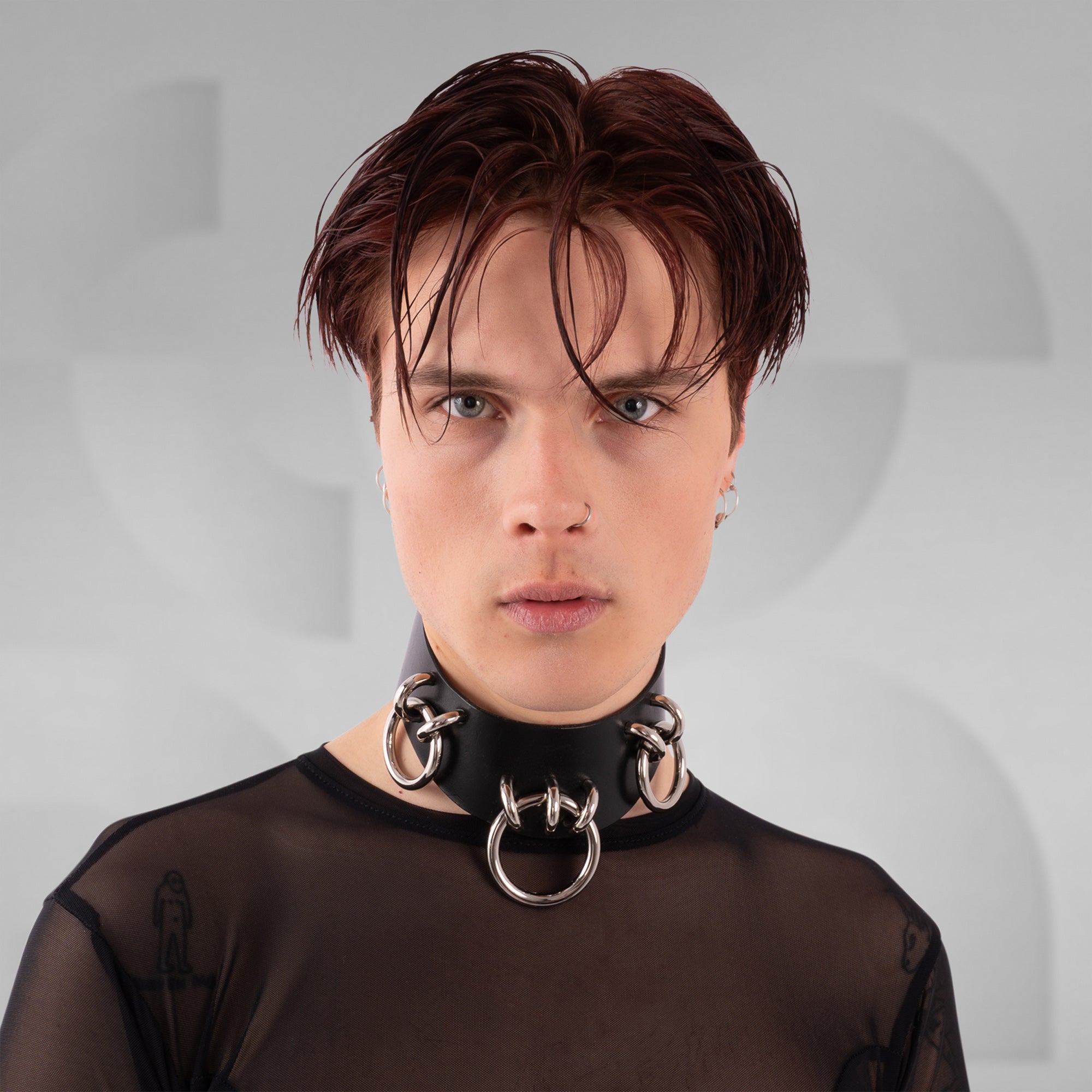 Person wearing a black garment with a large metallic choker against a gray background