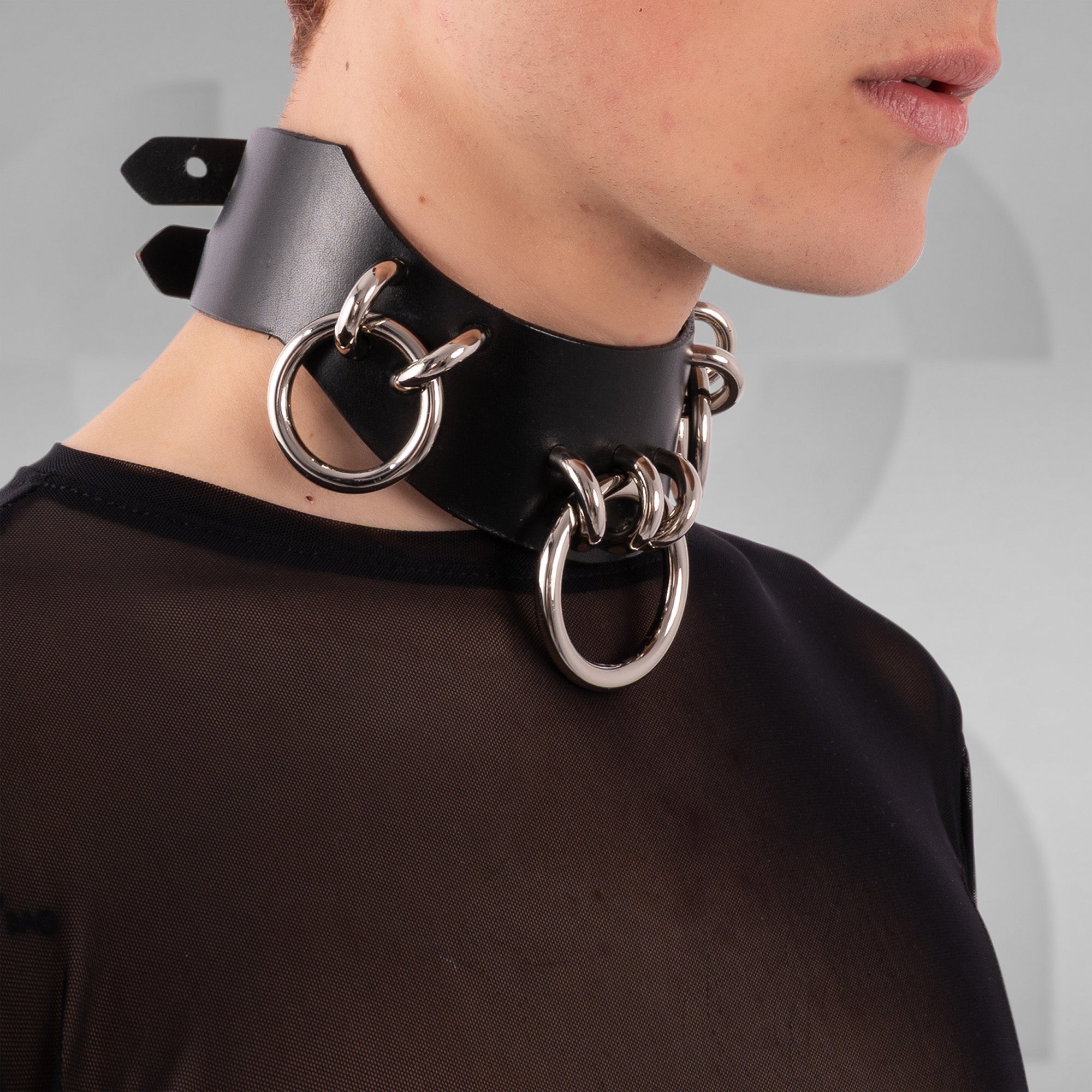 Person wearing a black leather choker with silver rings on a plain background