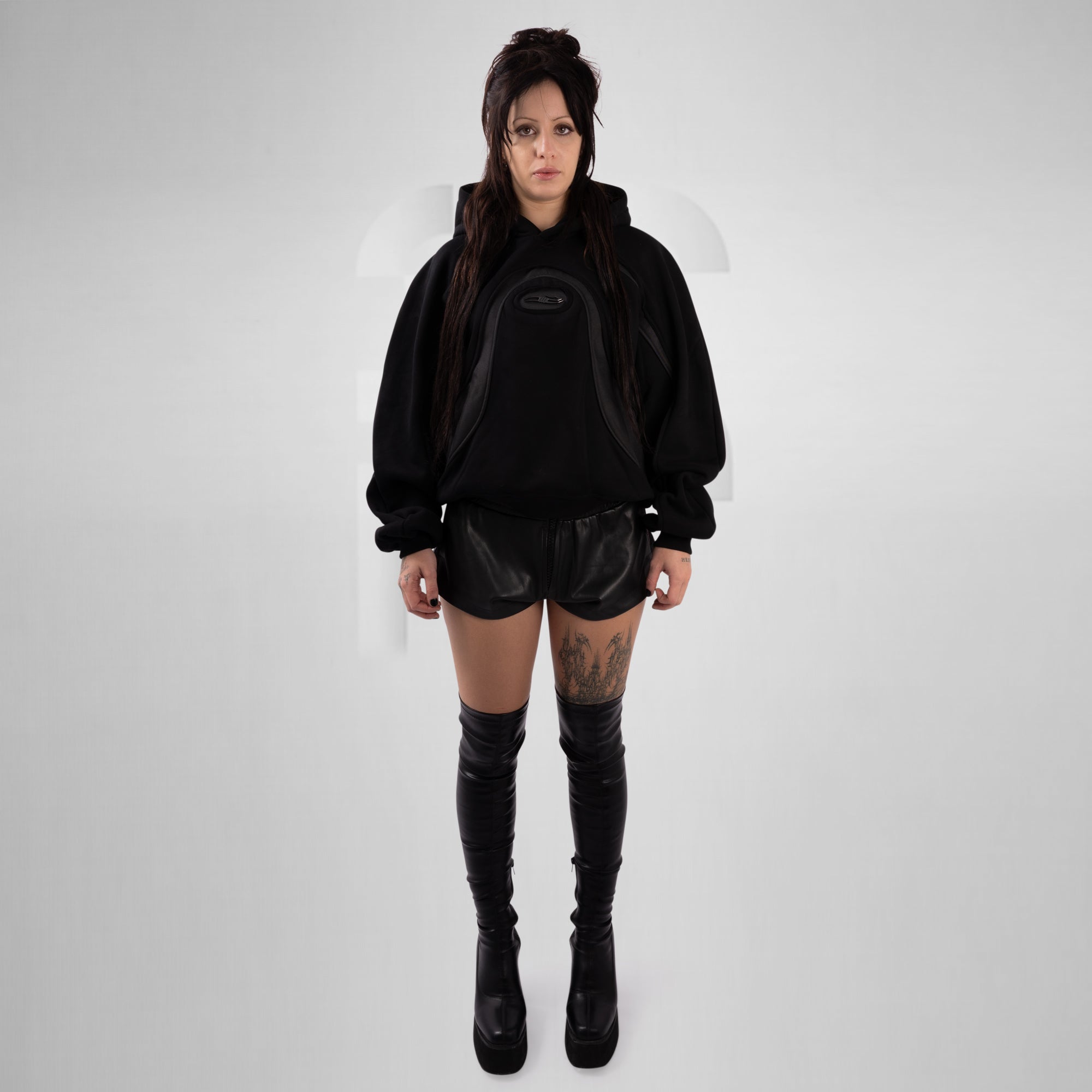 Person wearing a black hoodie, shorts, and knee-high boots on a white background
