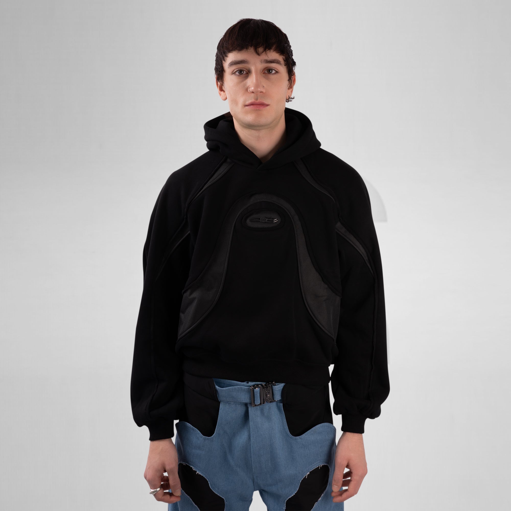 Person wearing a black hoodie with a unique design on a plain background