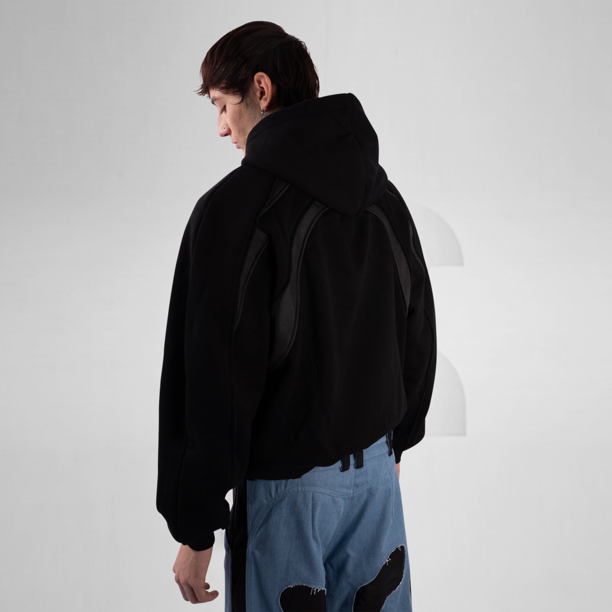 Person wearing a black hoodie and light blue pants on a white background