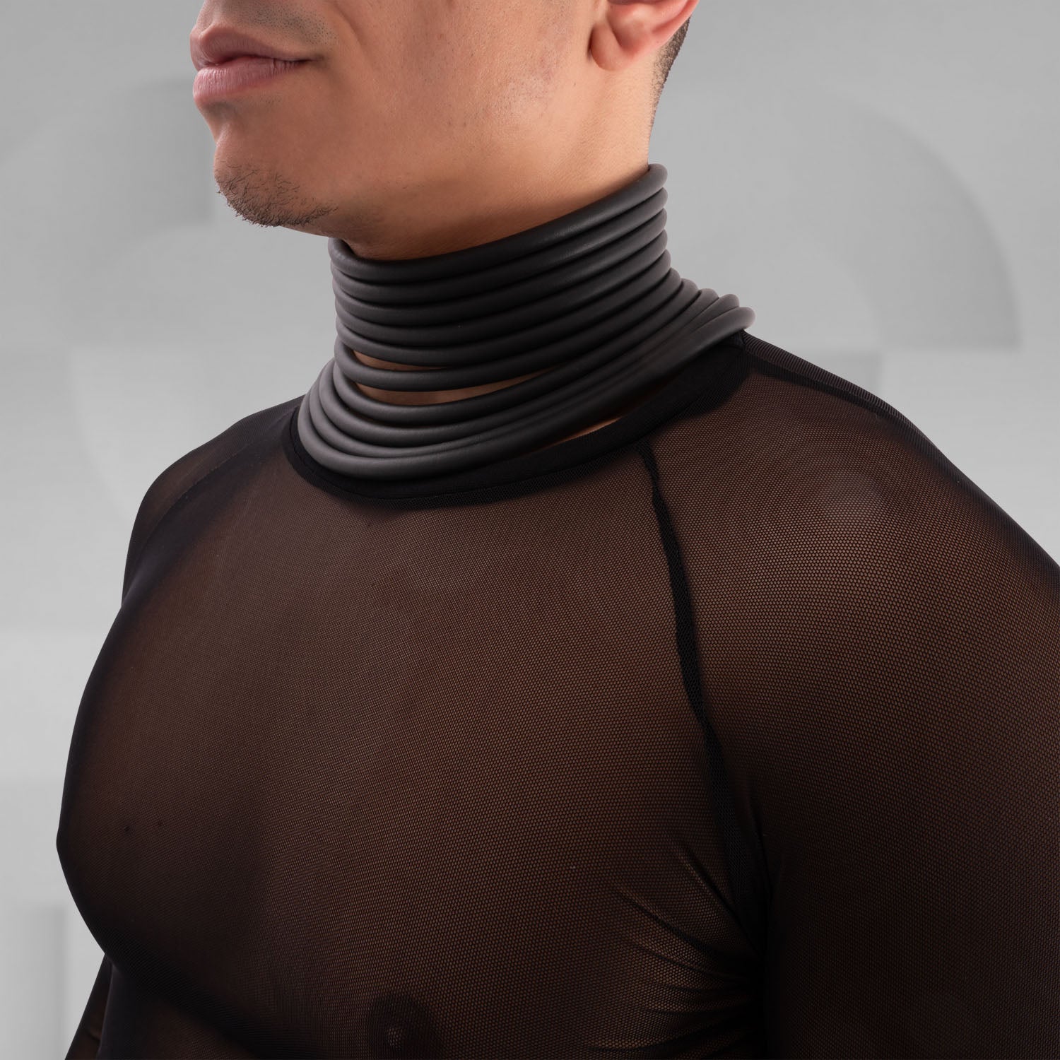 Model wearing a bold, futuristic black sheer long-sleeve top with a high neckline, paired with black cut-out shorts. The look is completed with a statement metallic choker and nipple pasties, creating an edgy, avant-garde aesthetic. Perfect for techno, festival, and alternative fashion