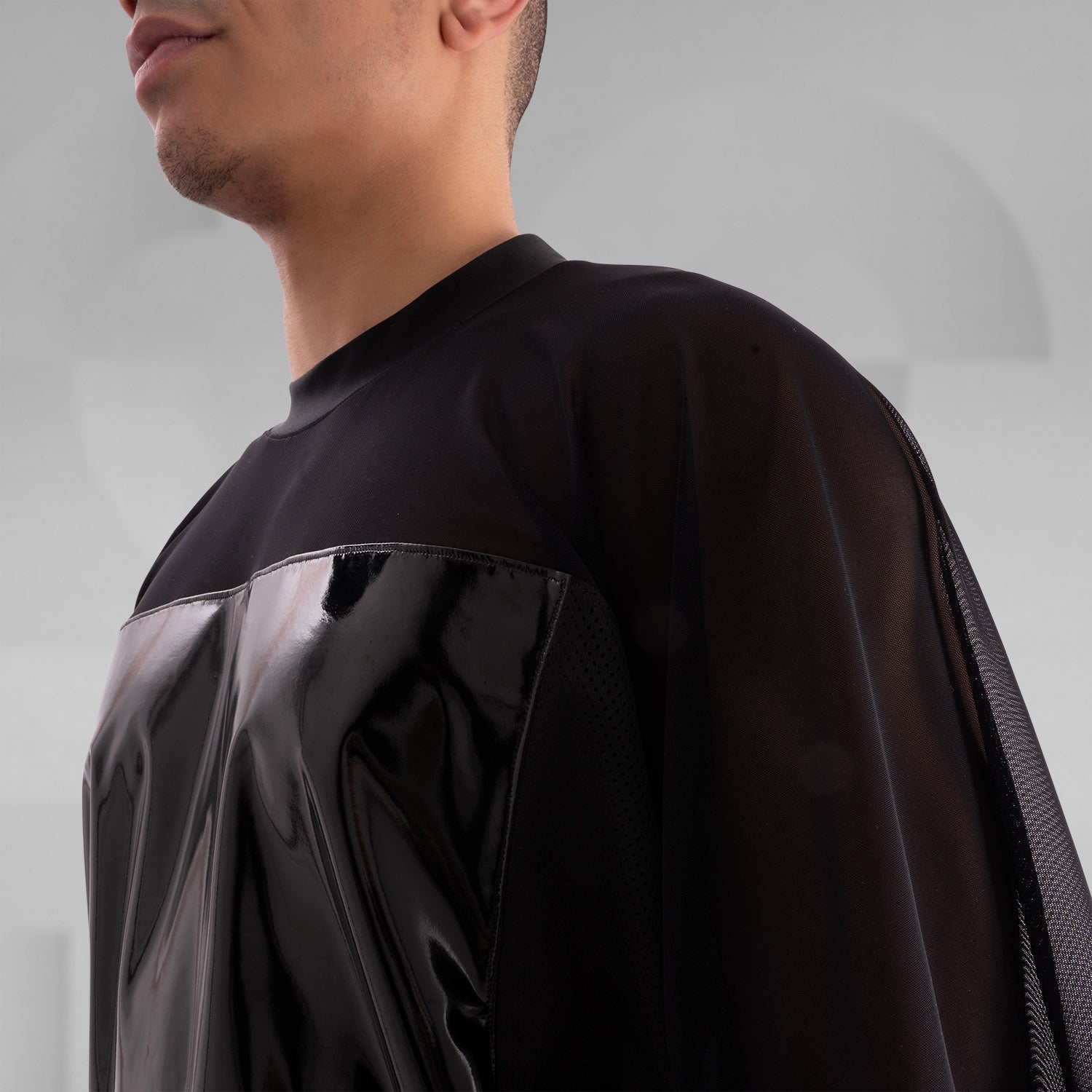 The image features a person wearing a striking outfit that combines a black, glossy top with sheer mesh sleeves, creating a bold and modern aesthetic. The top's shiny material adds an eye-catching element, while the coordinating shorts feature angular holographic designs that reflect light beautifully. This look embodies a dynamic blend of avant-garde fashion and street style, perfect for making a statement.