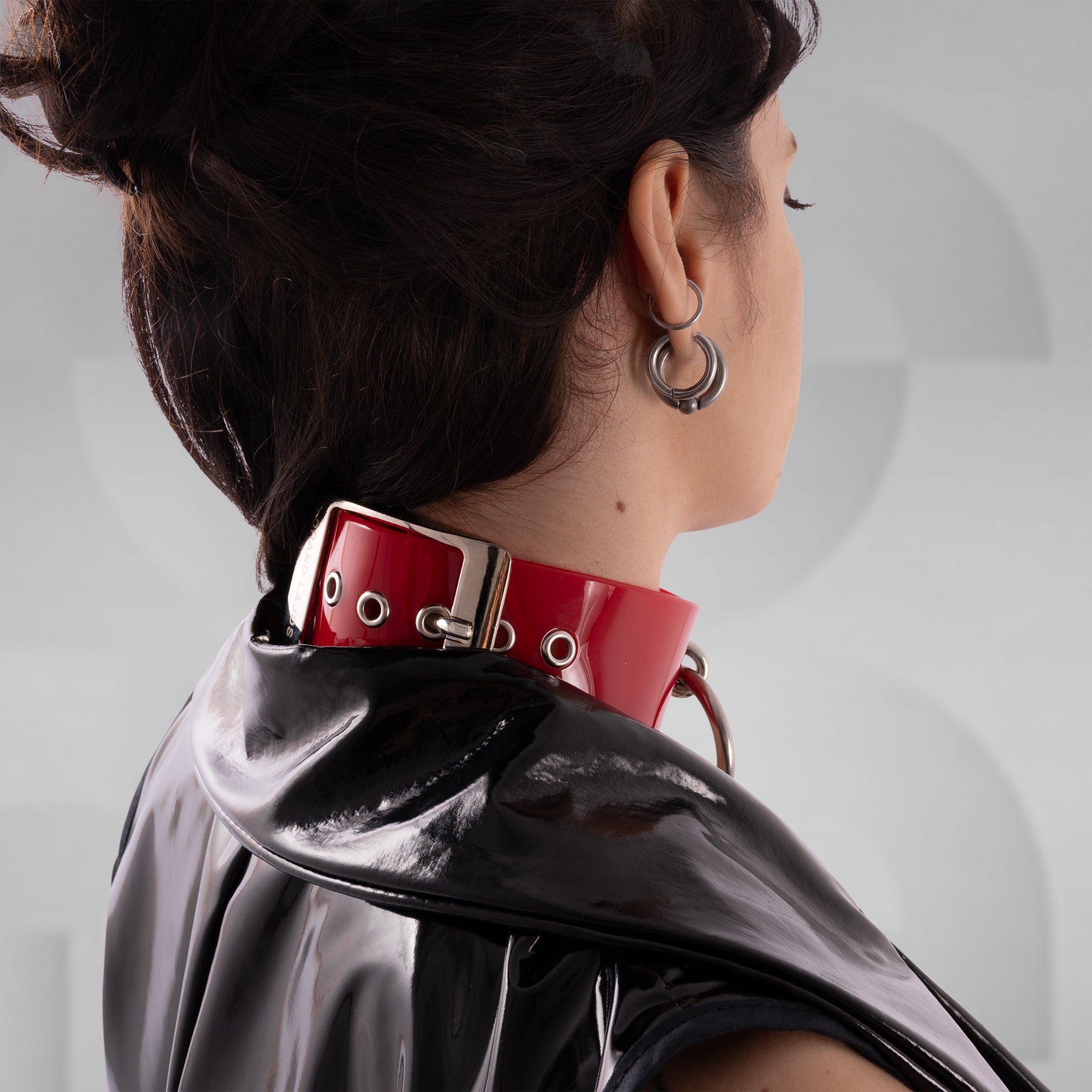 Person wearing a red choker with a metallic clasp on a plain background