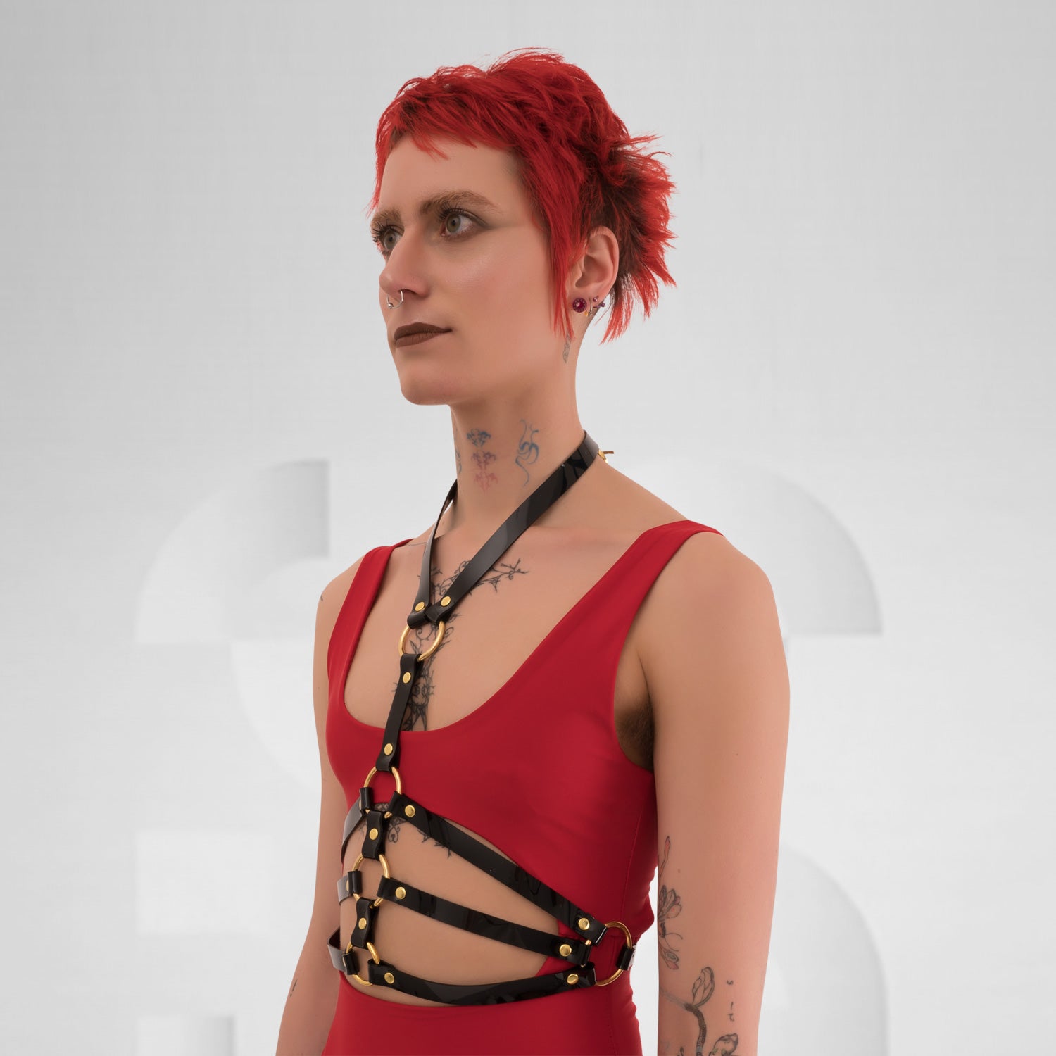 This image showcases a model wearing a striking black harness top that features a combination of sleek straps and bold detailing. The design includes eye-catching golden accents that enhance its edgy aesthetic, perfectly blending style and attitude. Crafted from high-quality materials, the harness contours the body beautifully while ensuring comfort and movement.