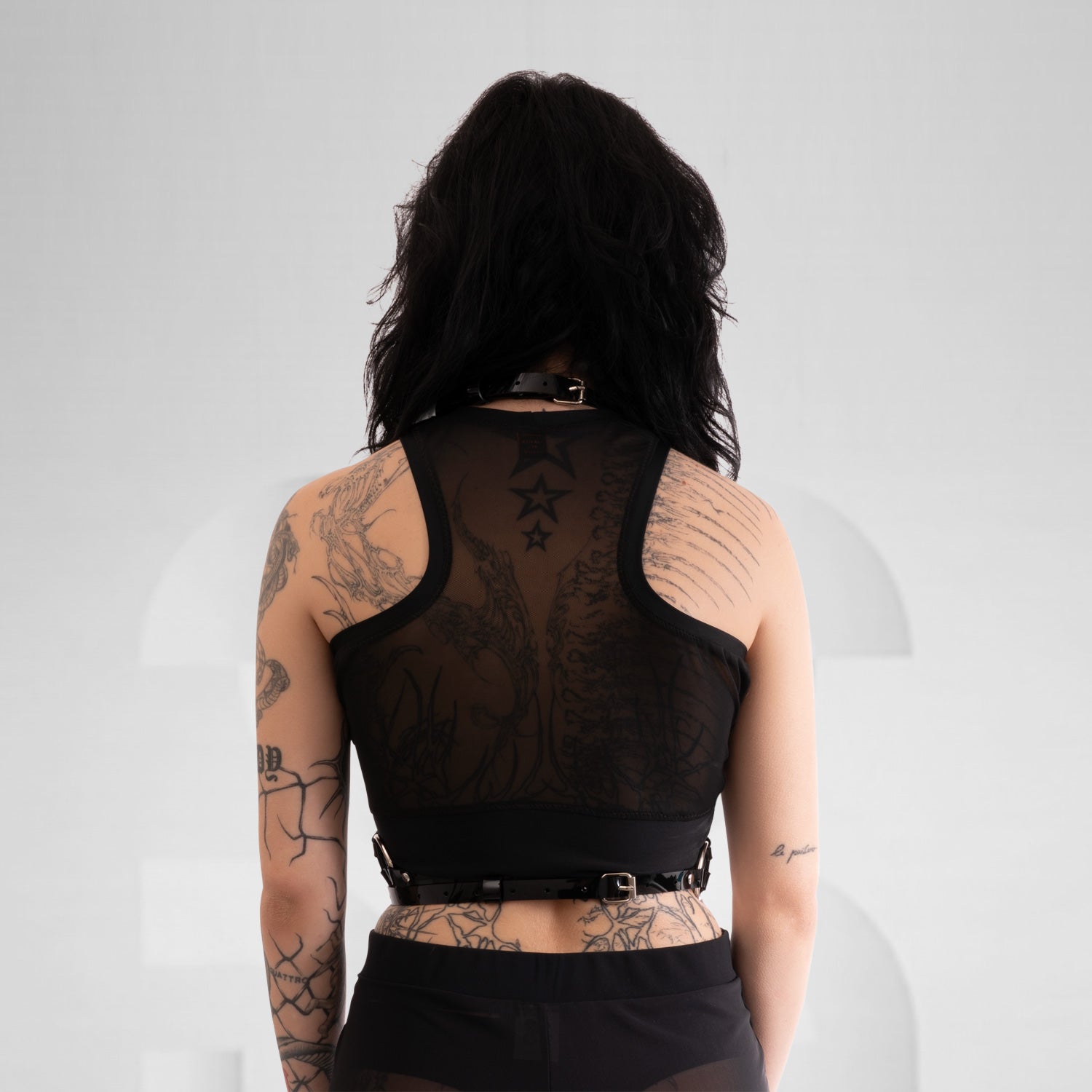 This image showcases a model wearing a striking black harness top that features a combination of sleek straps and bold detailing. The design includes eye-catching golden accents that enhance its edgy aesthetic, perfectly blending style and attitude. Crafted from high-quality materials, the harness contours the body beautifully while ensuring comfort and movement.