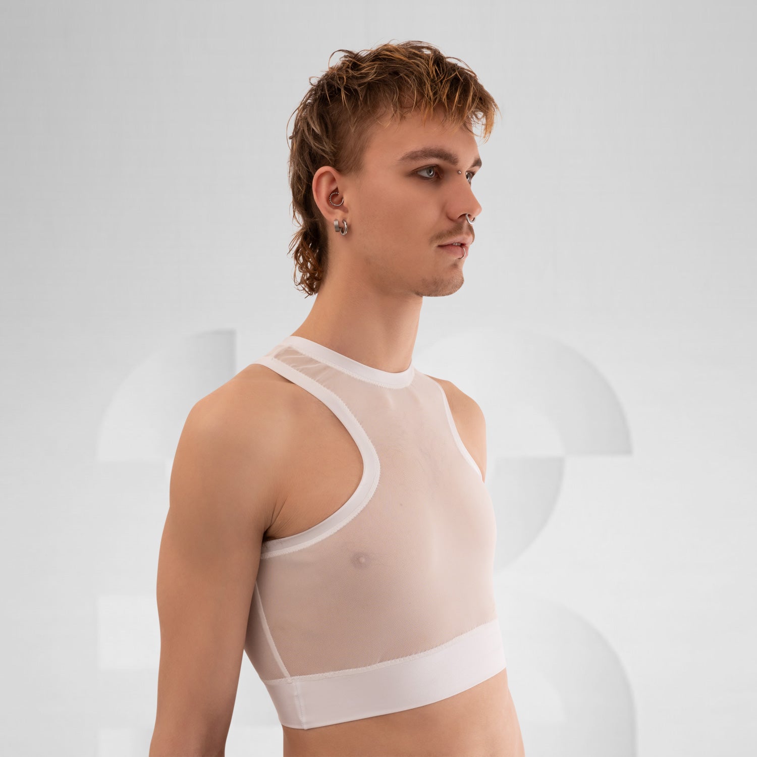 The side profile of a model wearing a translucent white top with a modern, sporty design. The top is complemented by a choker that has a gold detail, adding an edgy touch. The model has short, vibrant red hair and dramatic makeup, enhancing their bold look. The neutral background focuses attention on the outfit and the striking features of the model.