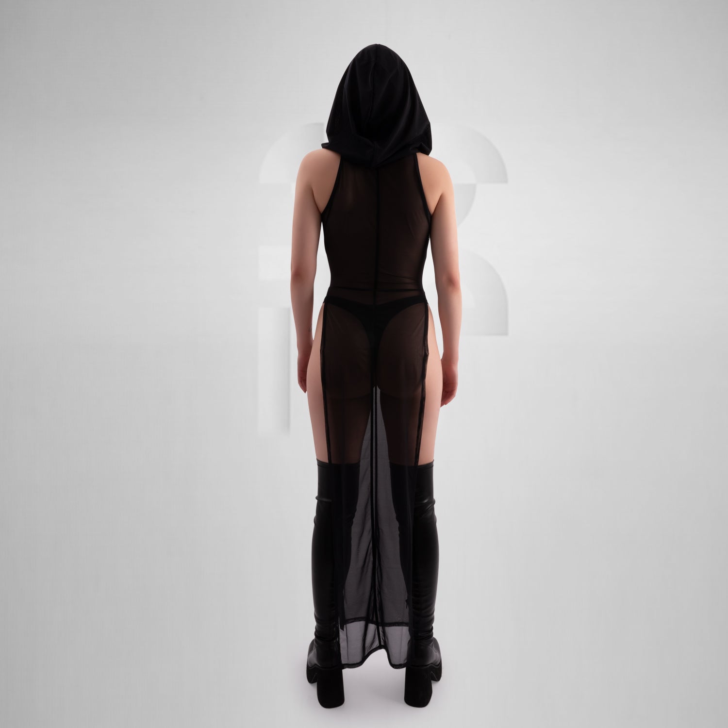 Model wearing a sheer black hooded dress with keyhole chest detail, belted at the waist with a chunky chain-accented rubber belt, paired with black platform boots and visible black lingerie — edgy, gothic-inspired look perfect for clubwear or alternative fashion.