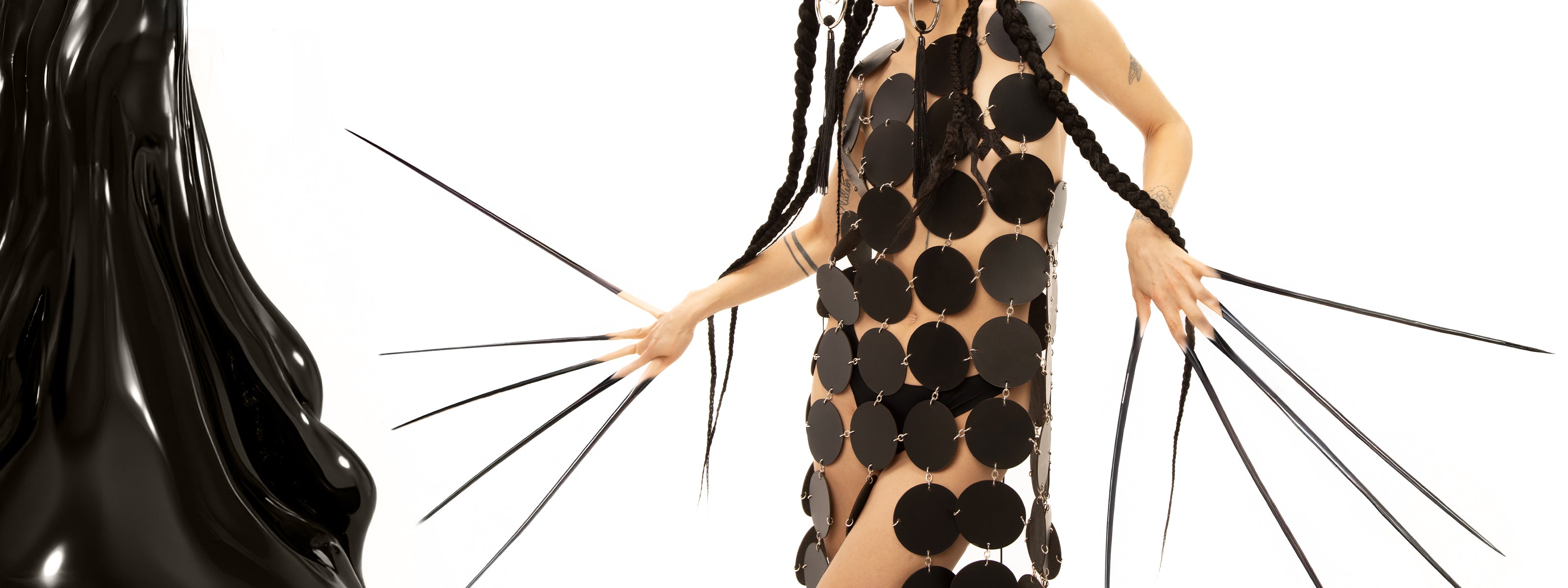 girl exudes an air of intrigue with her long, dramatic nails and a striking avant-garde black dress that flows with an artistic flair. Her long, intricately braided hair adds a touch of elegance, complementing her bold style and creating a mesmerizing silhouette that turns heads wherever she goes.