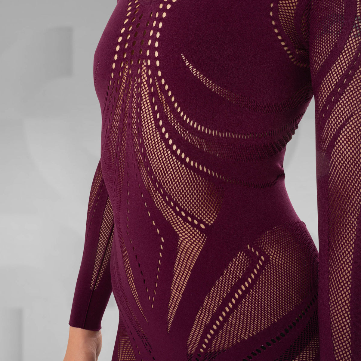 Close-up of a burgundy long-sleeve knit dress with an intricate openwork geometric pattern, shown on a model against a neutral gray background.