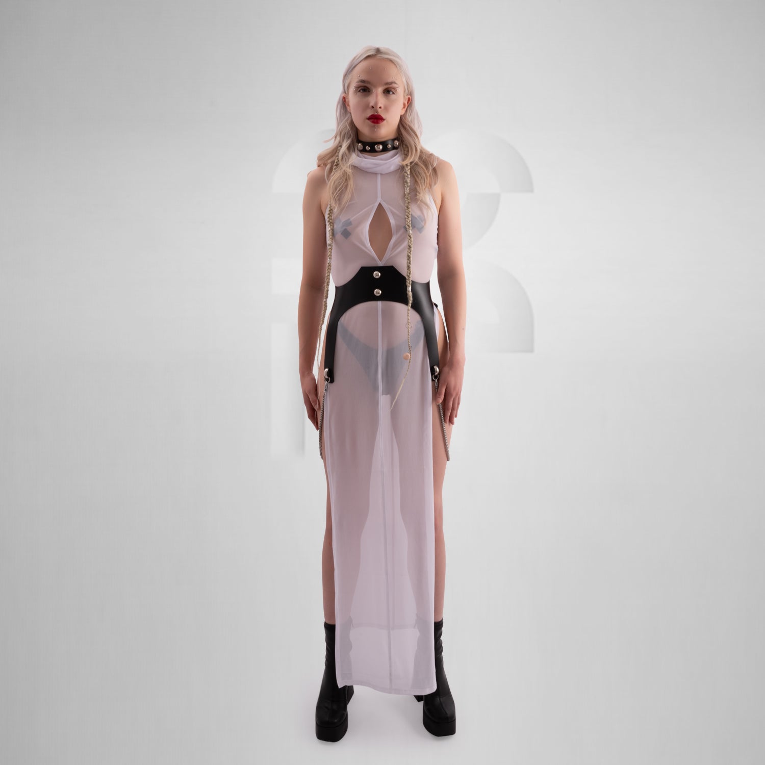 The image features a sheer, long white dress with a high neckline, front zipper, and side slits, paired with chunky black boots. The dress has a futuristic, edgy vibe, combining elegance with boldness.