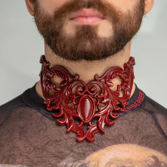  of an ornate, red choker featuring intricate decorative patterns. The choker's elaborate design adds a touch of elegance and drama, perfectly complementing the sophisticated look. The focus on the choker against the subtle background highlights its detailed craftsmanship and striking style.