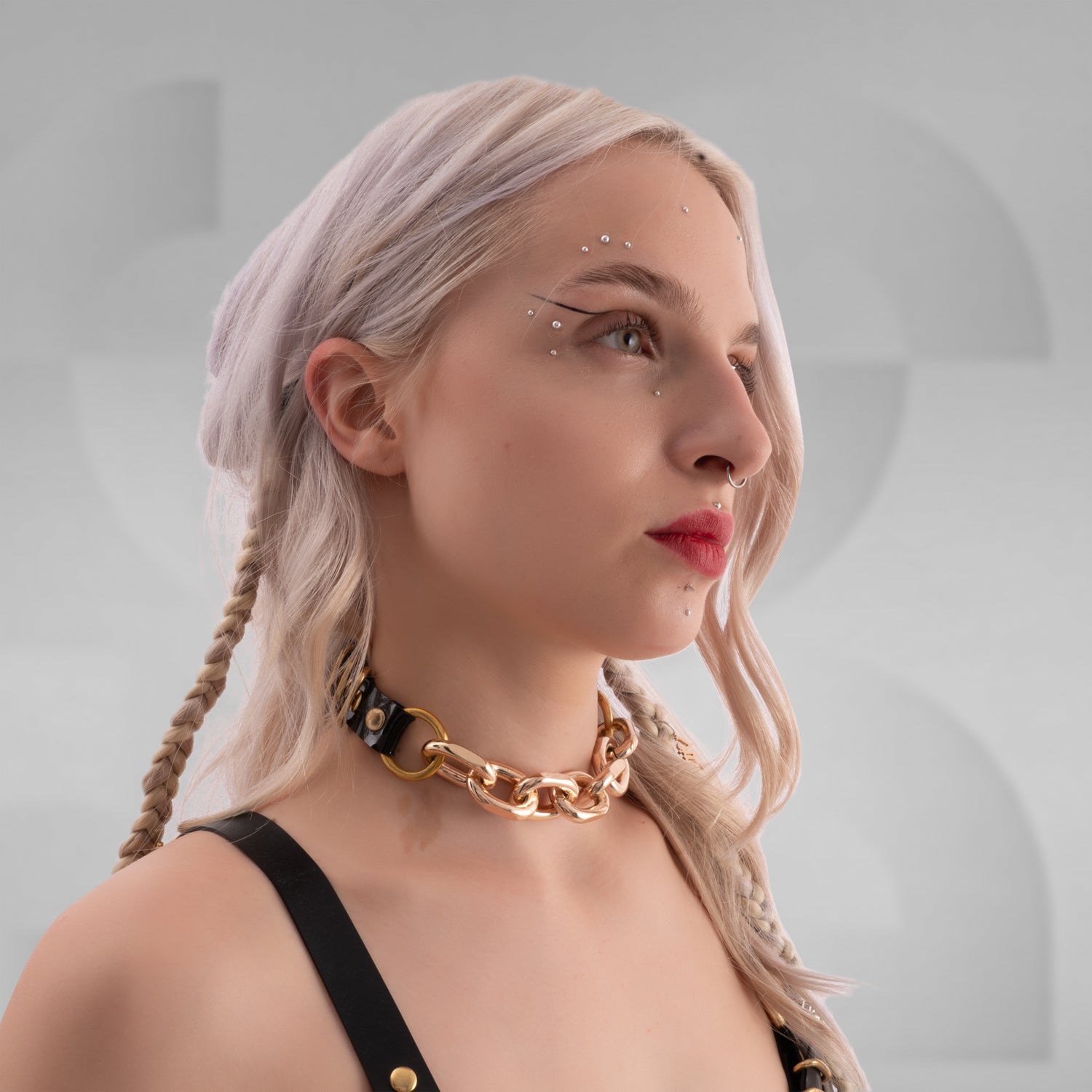 The chain or product shown in the images is a fashion choker and harness made of black material with large gold-colored metal links, rings, and buckles. The design features a combination of chunky links and smaller straps with adjustable buckles, creating an edgy and bold accessory look.