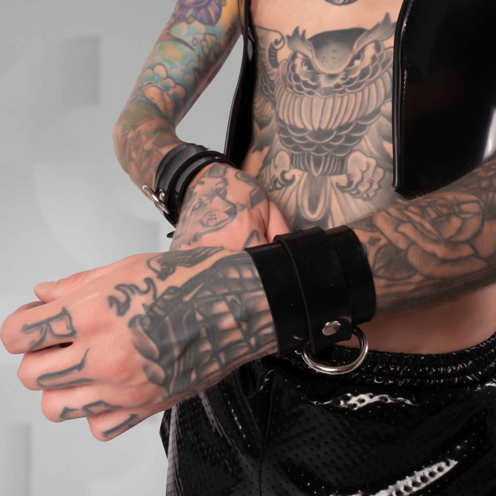 Person with tattoos wearing a black leather glove and bracelet on a plain background