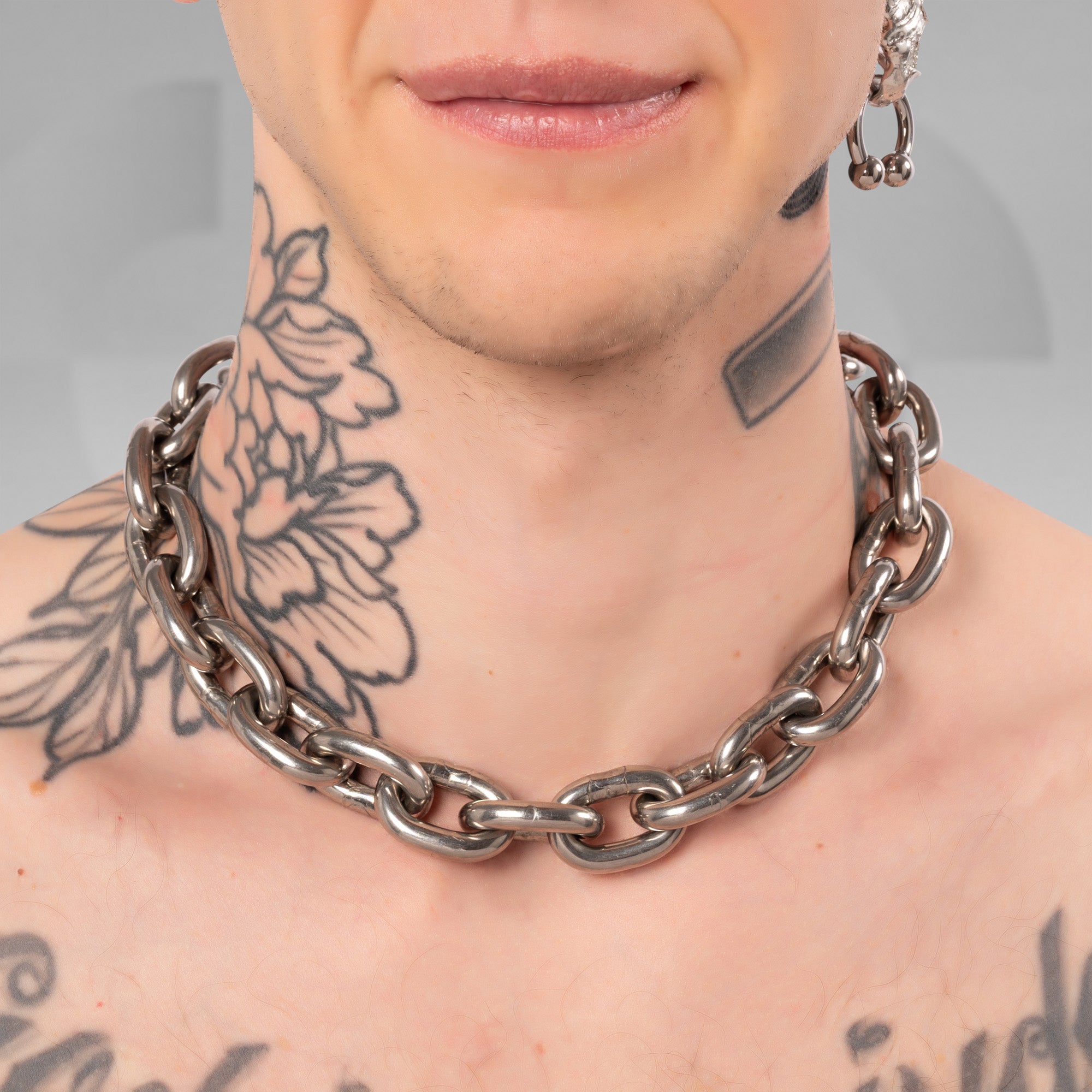 A close-up of a person's neck and upper chest wearing a chunky, polished silver-tone chain necklace with large interlocking links.