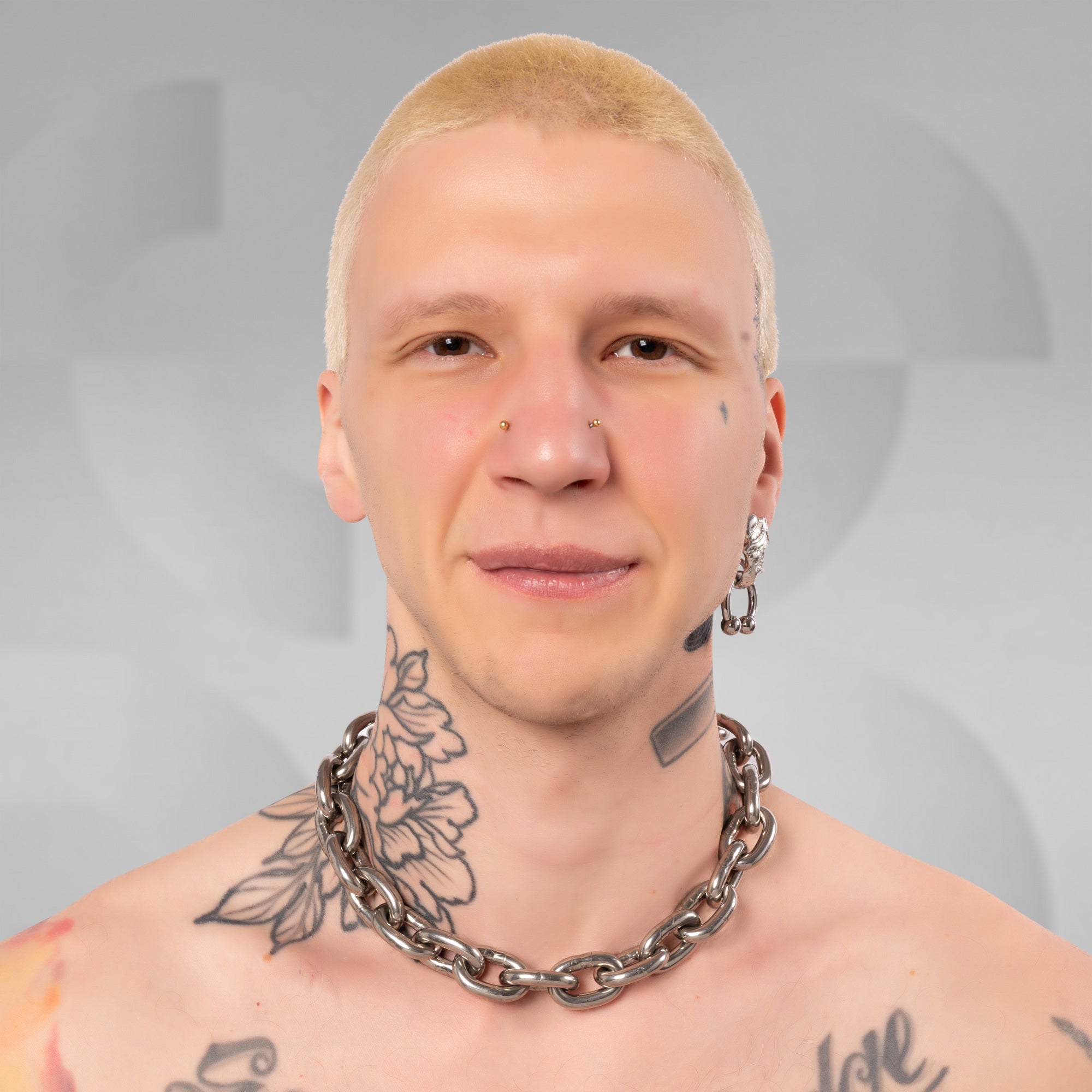 A close-up portrait of a man with a buzz cut, wearing a chunky silver chain necklace and a silver hoop earring, against a gray background with a faint circular logo.