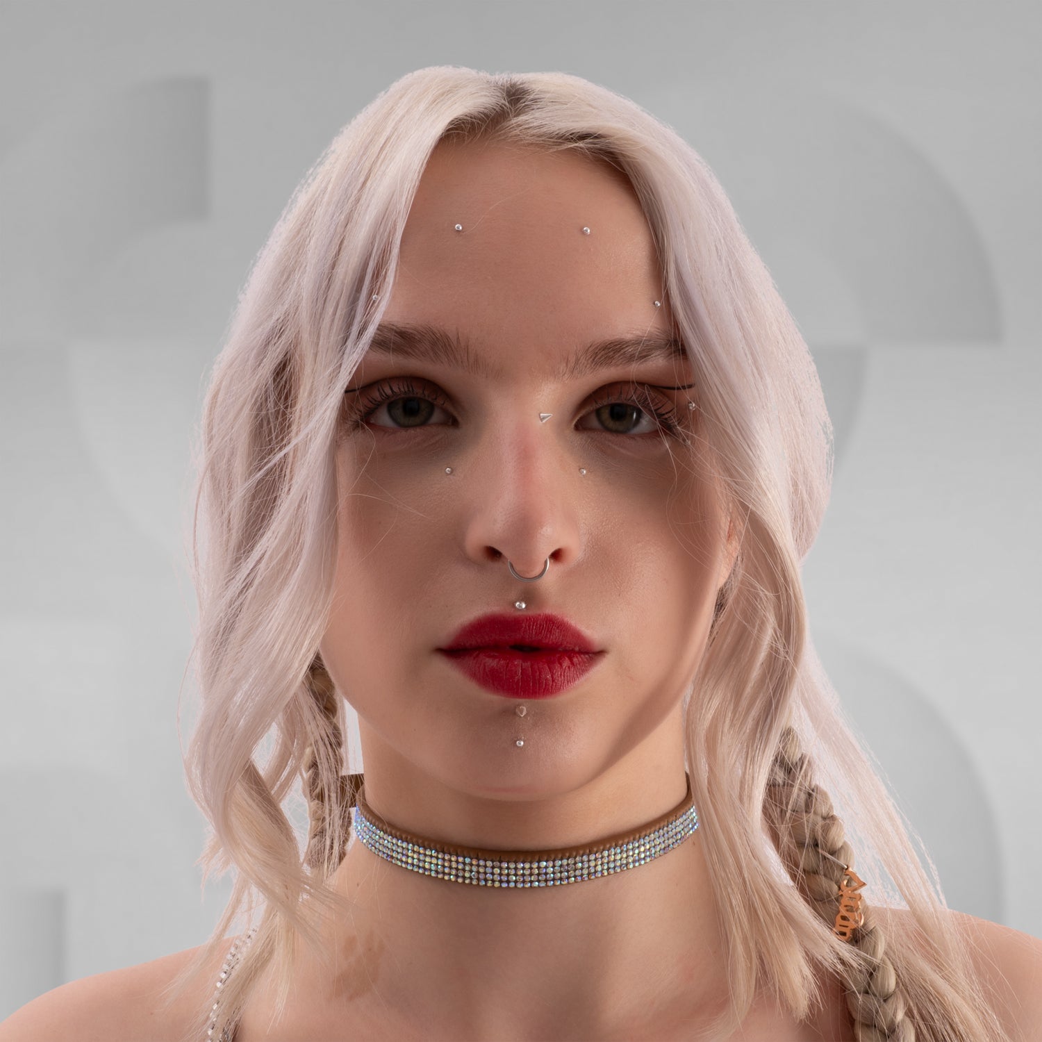 In this picture, you can see a close-up of a woman wearing a striking white rhinestone choker around her neck, which adds a glamorous and edgy vibe. She has platinum blonde hair styled with soft waves, and a small braid on one side. Her makeup features bold red lipstick that matches her choker, and she has a septum piercing as well as two dermal piercings below her lips, adding to her alternative, fashionable style. 
