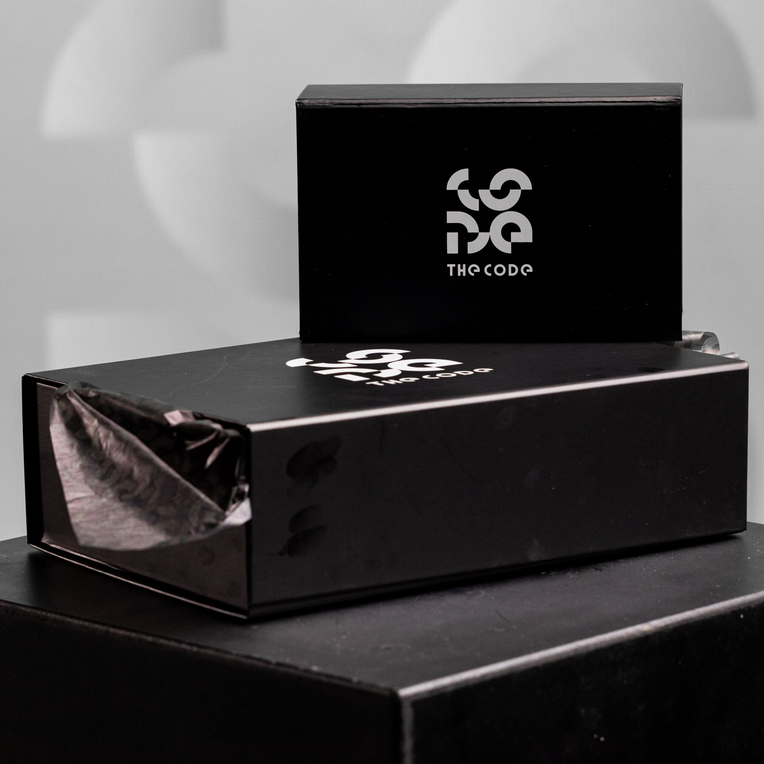 The image showcases elegant packaging from The Code, featuring a sleek black box adorned with the brand's distinctive logo. This refined presentation reflects the sophistication and style of the products inside, making it perfect for gifting or personal indulgence. The attention to detail in the packaging embodies The Code's commitment to quality and avant-garde fashion, ensuring a memorable unboxing experience that aligns with the edgy aesthetics of the brand.