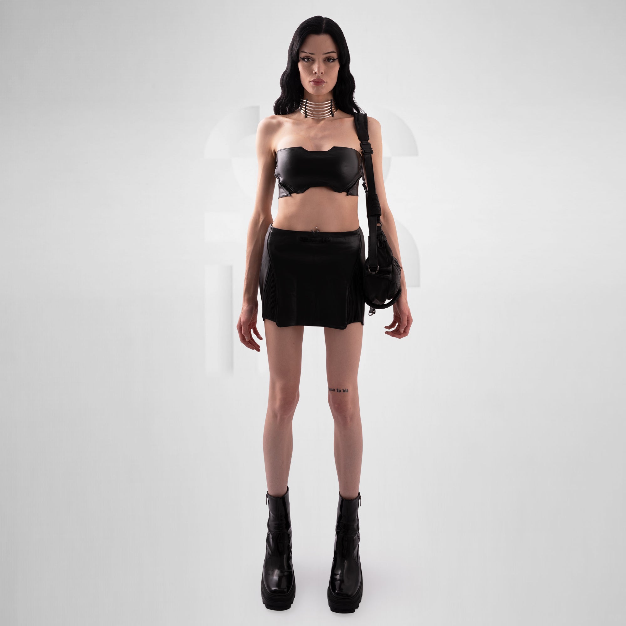 Person wearing a black outfit with a top, skirt, and boots on a white background