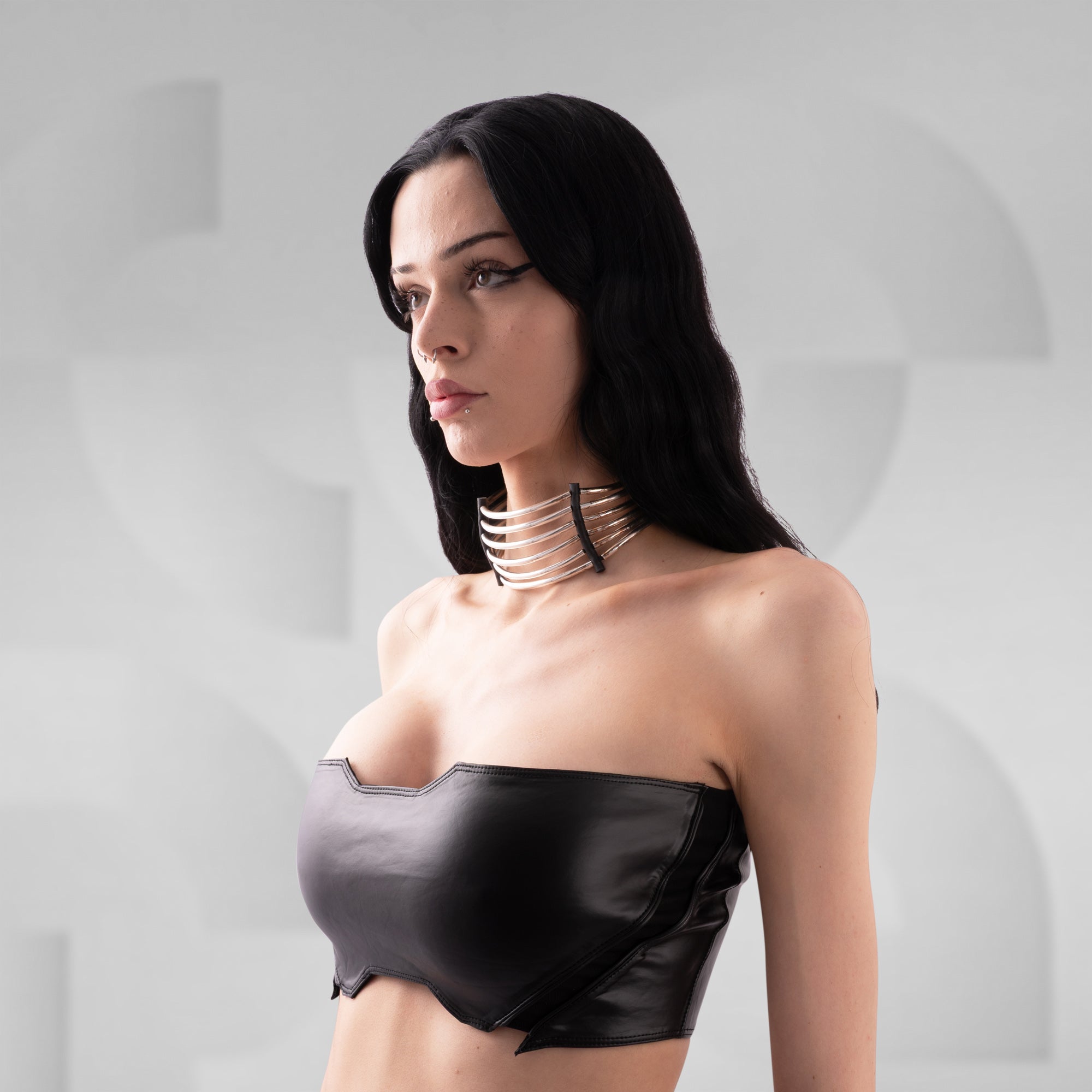 Woman wearing a black strapless top and multiple necklaces against a gray background