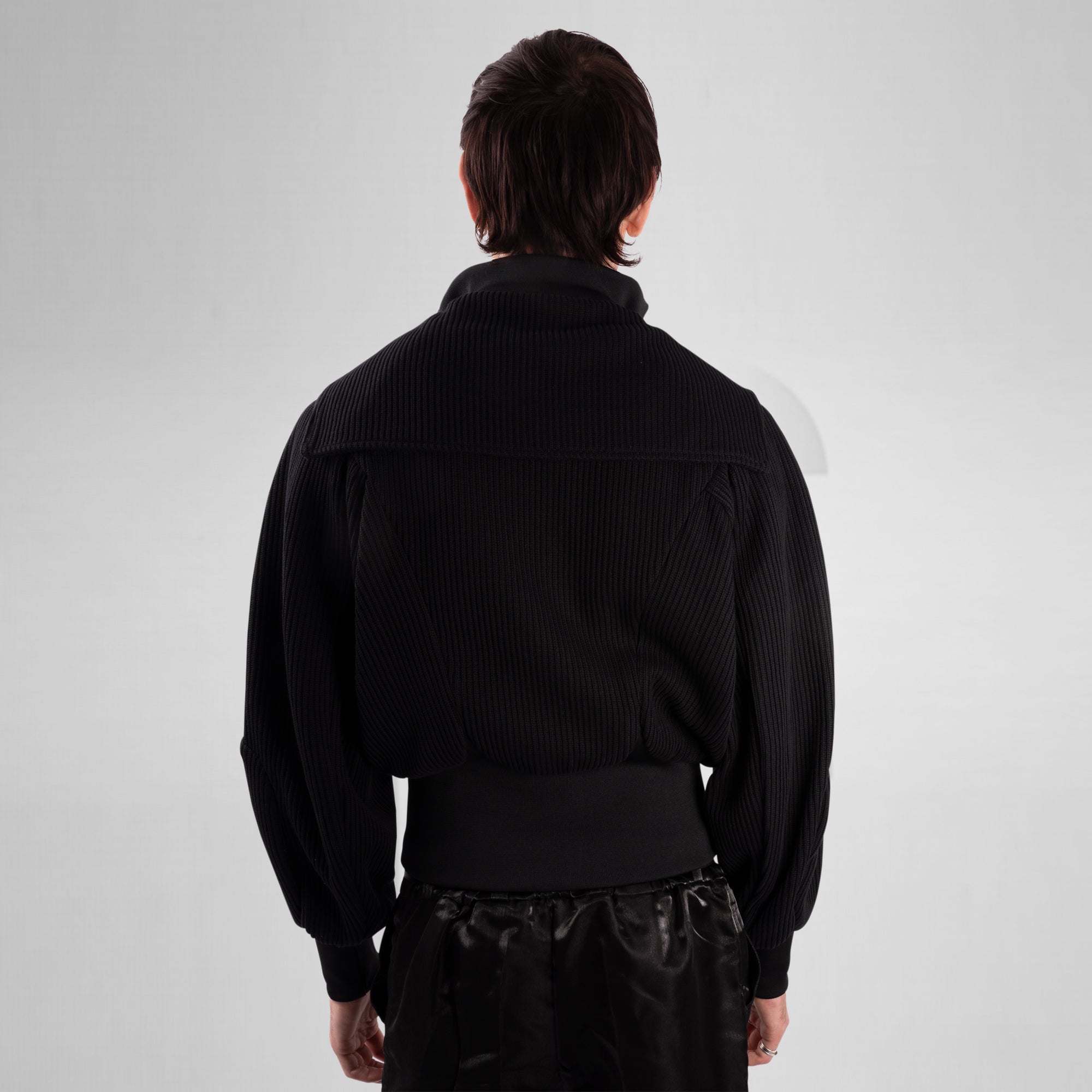 Person wearing a black ribbed sweater on a white background