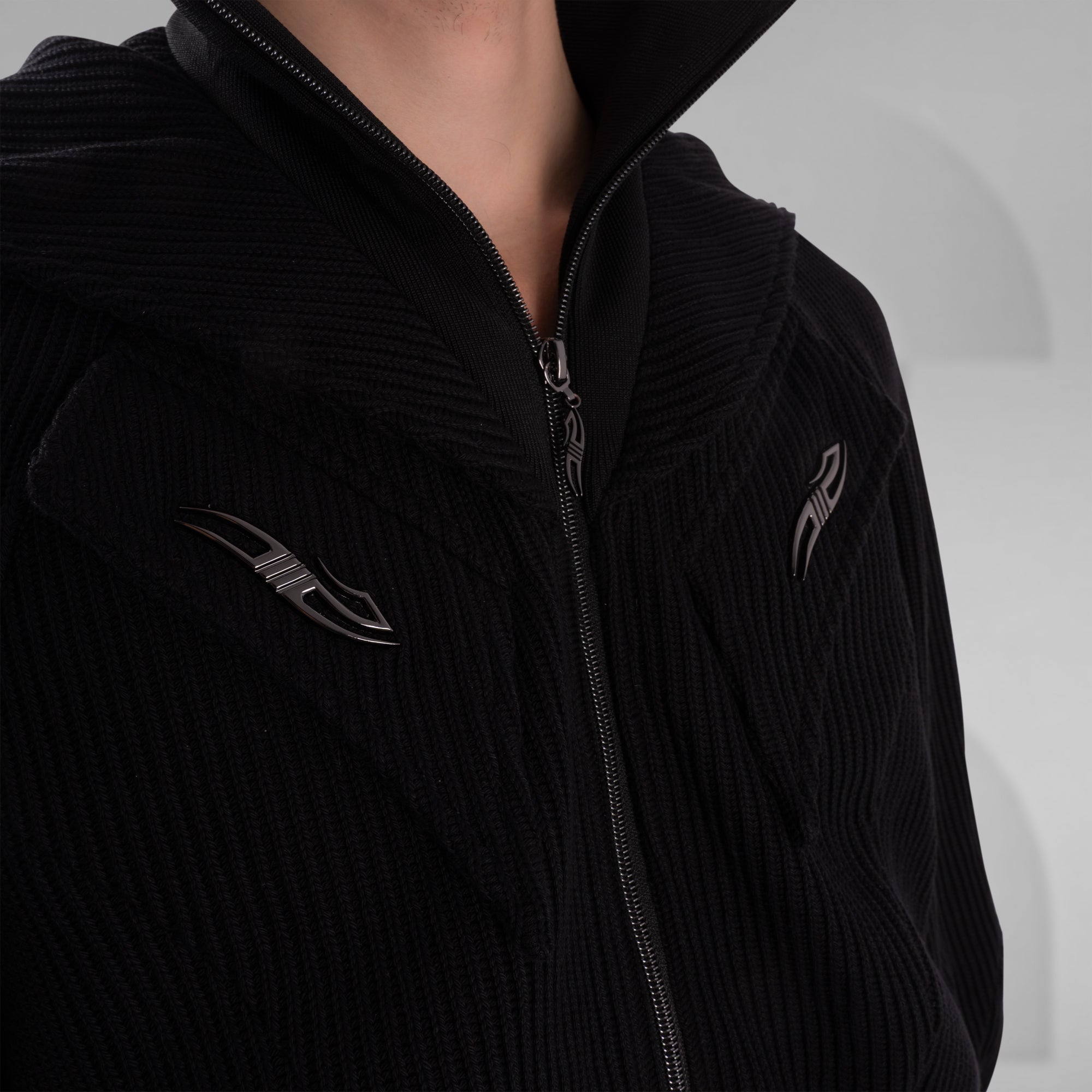 Black jacket with zipper and embroidered logo on a neutral background